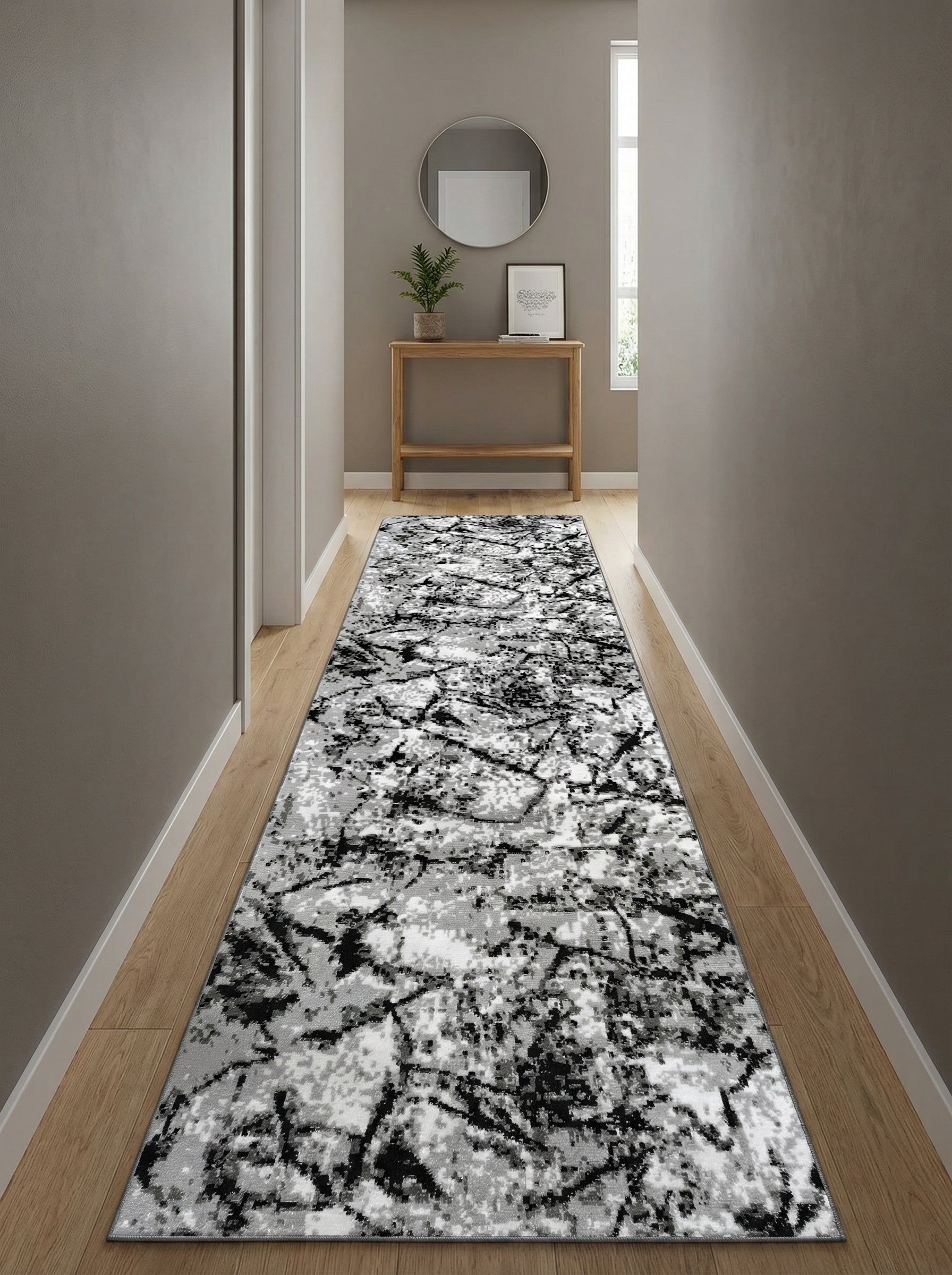 Tapis de couloir rectangulaire à motifs abstraits noirs, gris et blancs, posé sur un parquet dans une entrée lumineuse