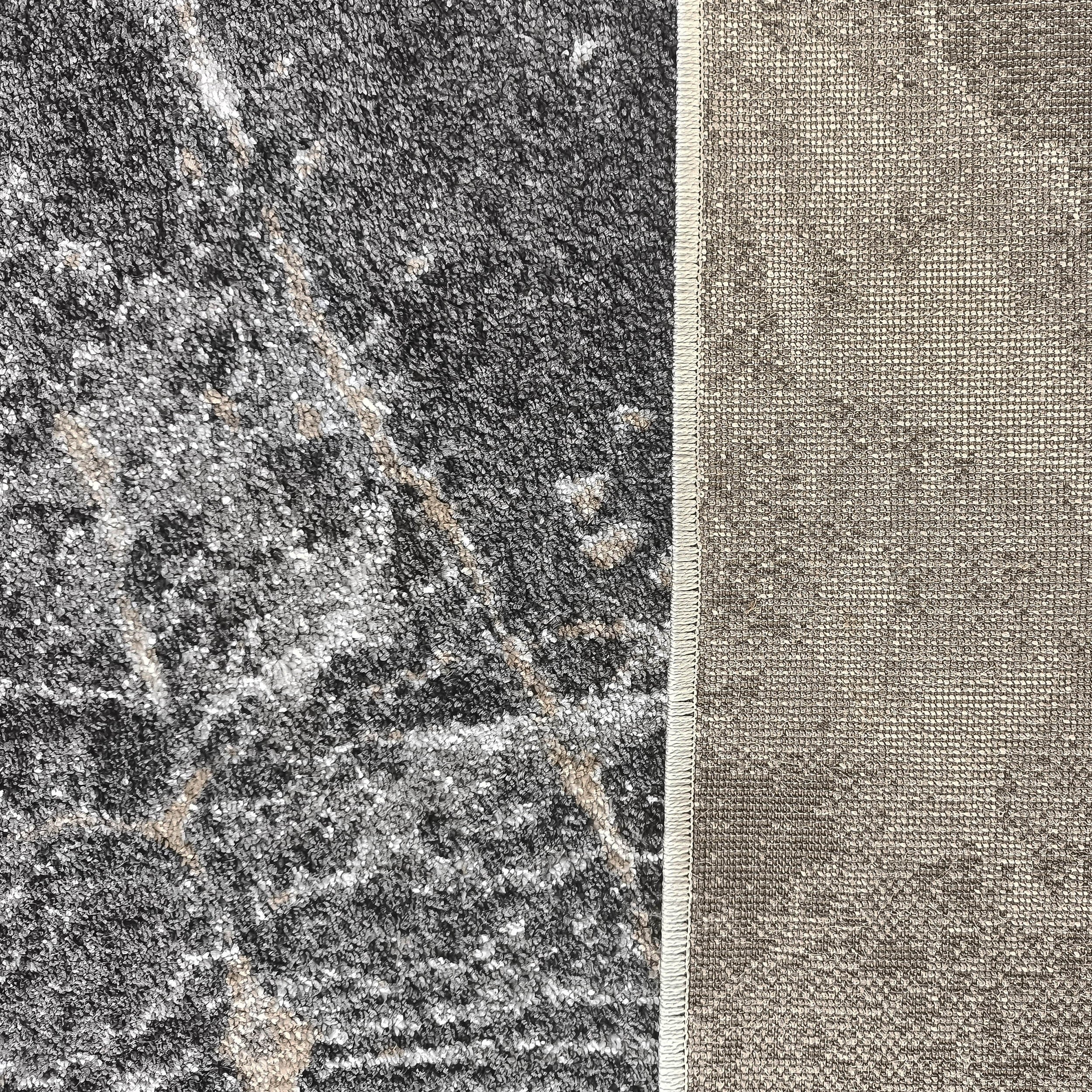 Dessus d'un tapis gris foncé moucheté de blanc et beige, avec un envers tissé beige et une bordure visible