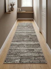 Tapis de couloir rectangulaire gris, noir et blanc à motifs abstraits de planches usées, posé sur parquet clair dans un couloir