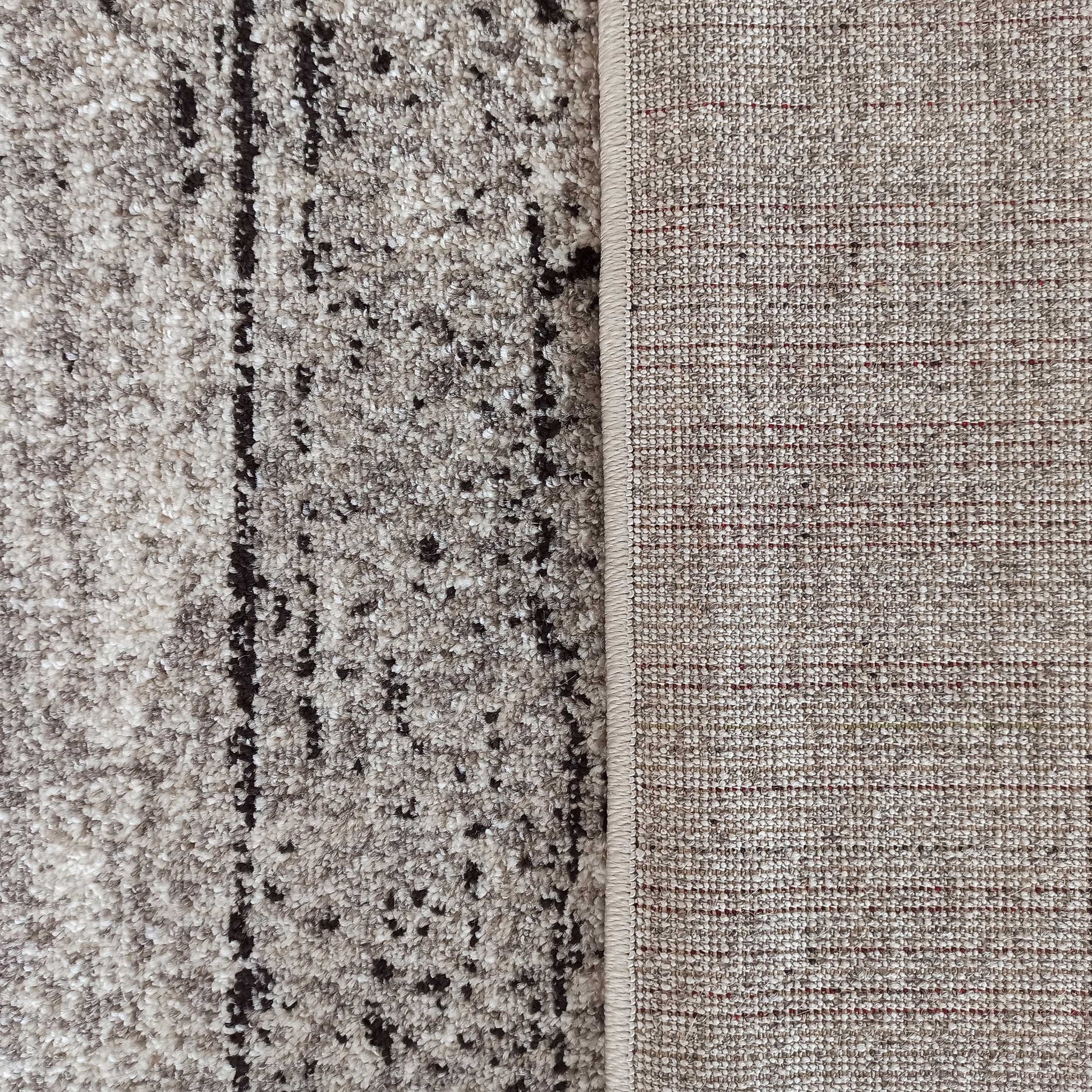 Tapis à la surface moelleuse beige et crème avec des motifs abstraits sombres, dont l'envers tissé est visible avec des fils rouges