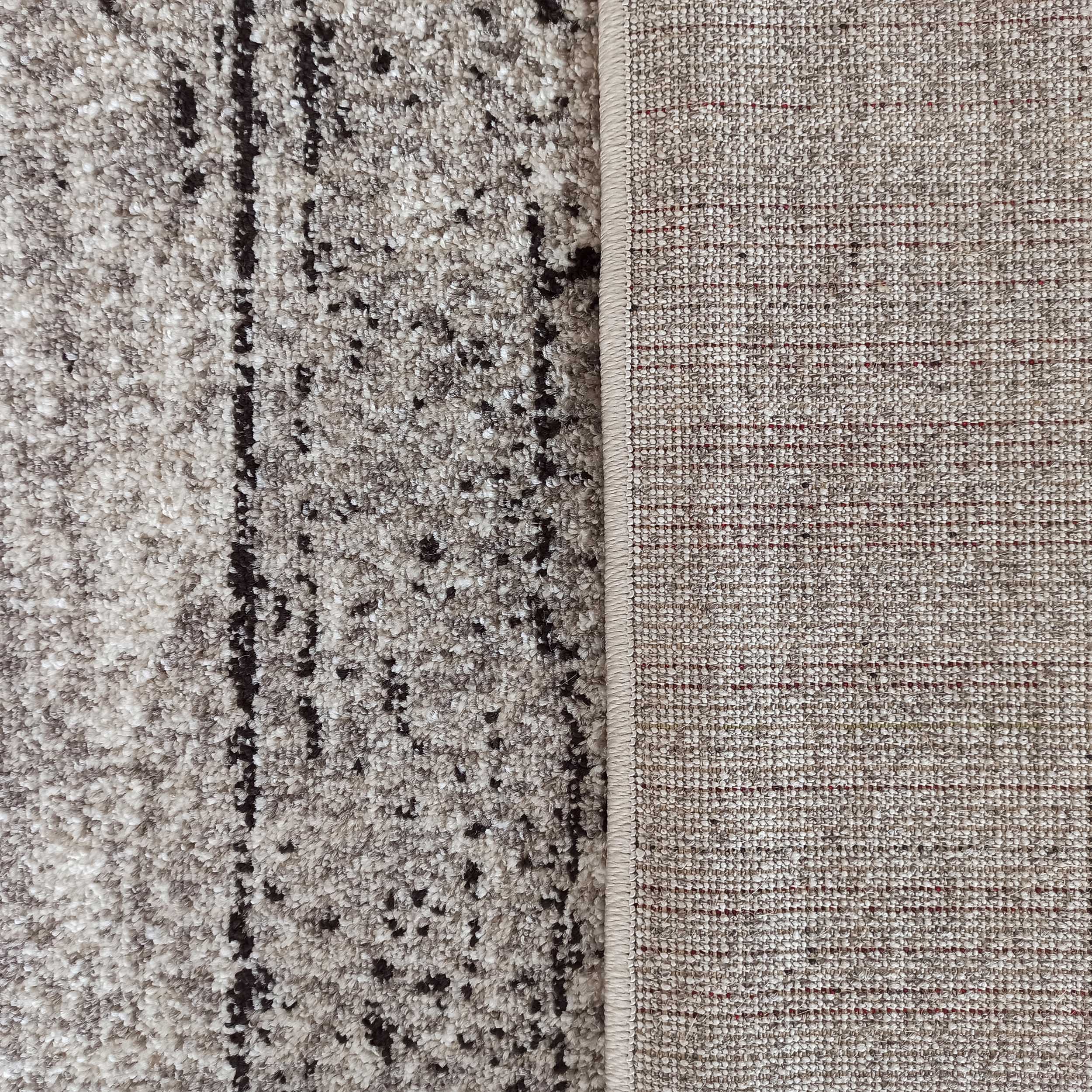 Tapis à la surface moelleuse beige et crème avec des motifs abstraits sombres, dont l'envers tissé est visible avec des fils rouges