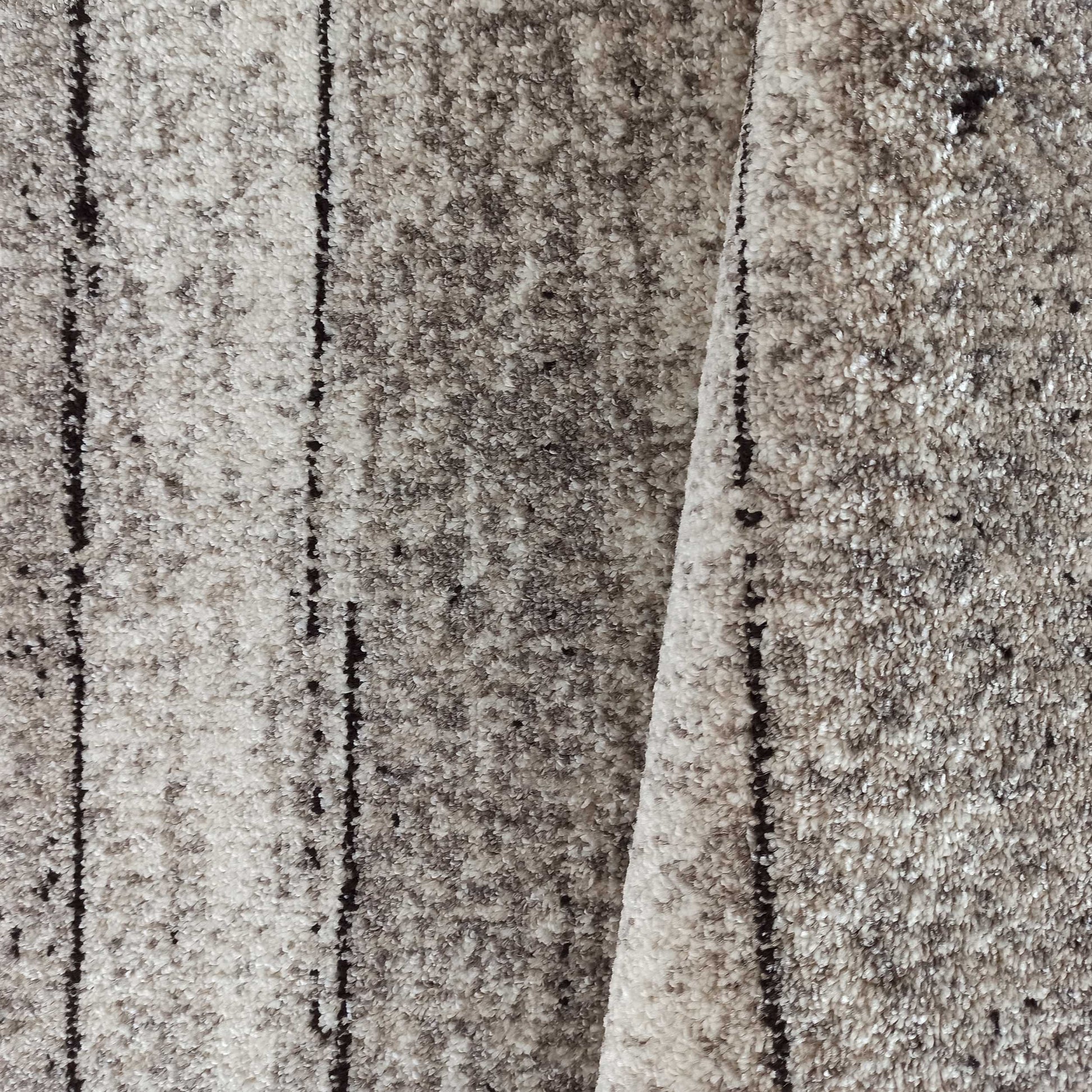 Tapis moelleux aux tons de gris clair et foncé, avec une texture tachetée et des lignes verticales noires irrégulières