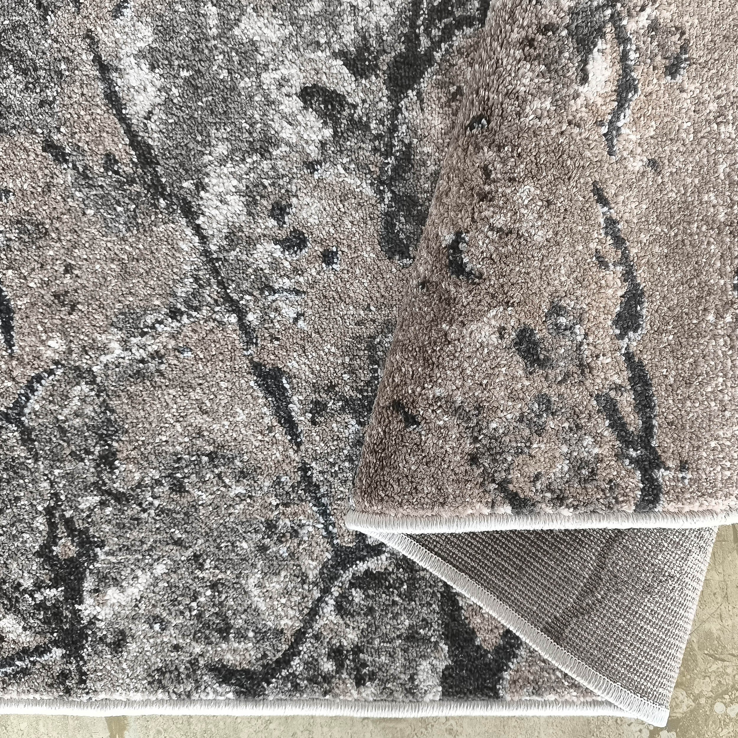 Tapis moelleux gris et beige aux motifs abstraits noirs et blancs, partiellement roulé, avec son envers texturé visible