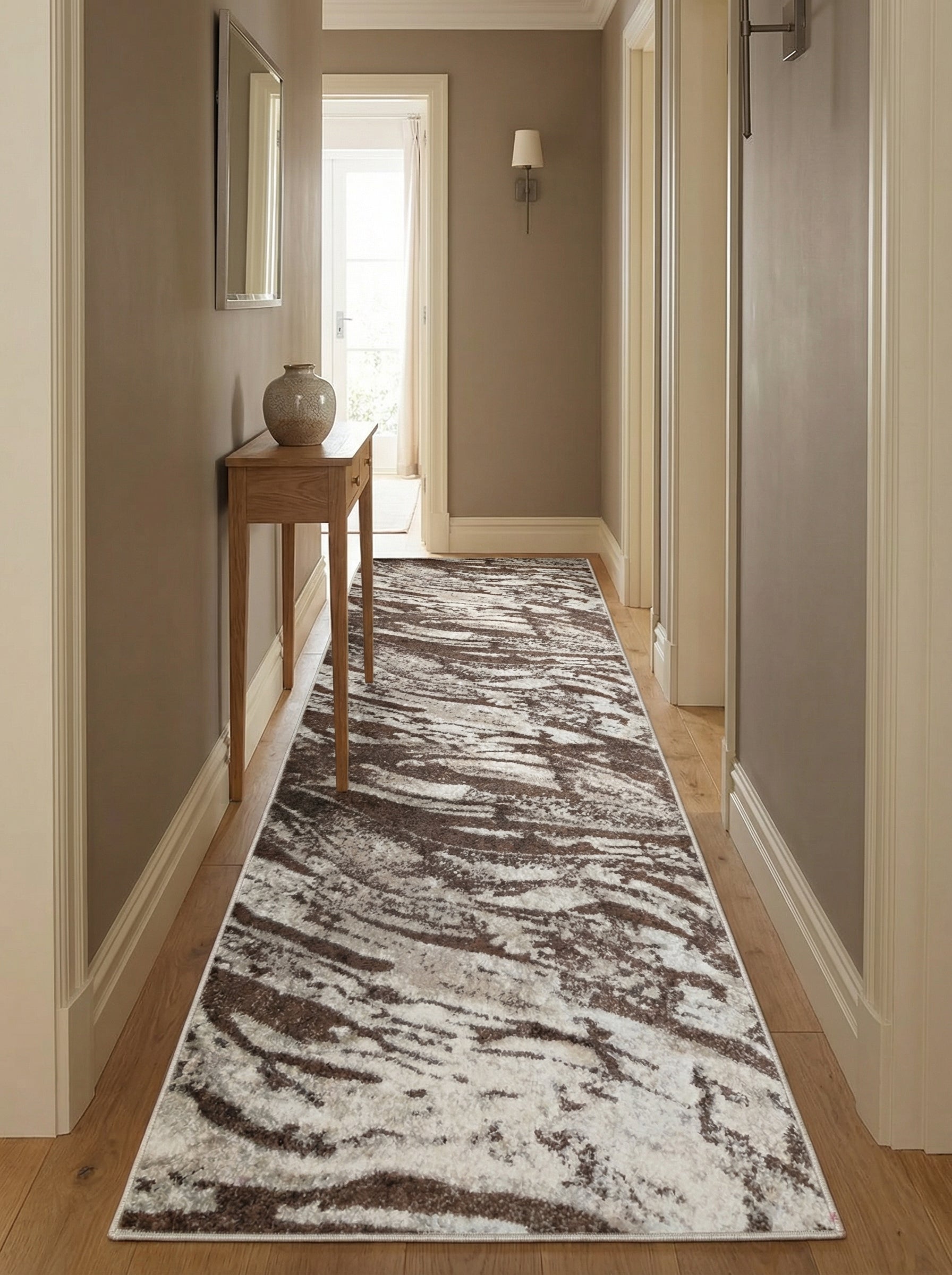 Tapis de couloir rectangulaire à motifs abstraits marron, gris et crème posé sur un parquet dans une entrée lumineuse