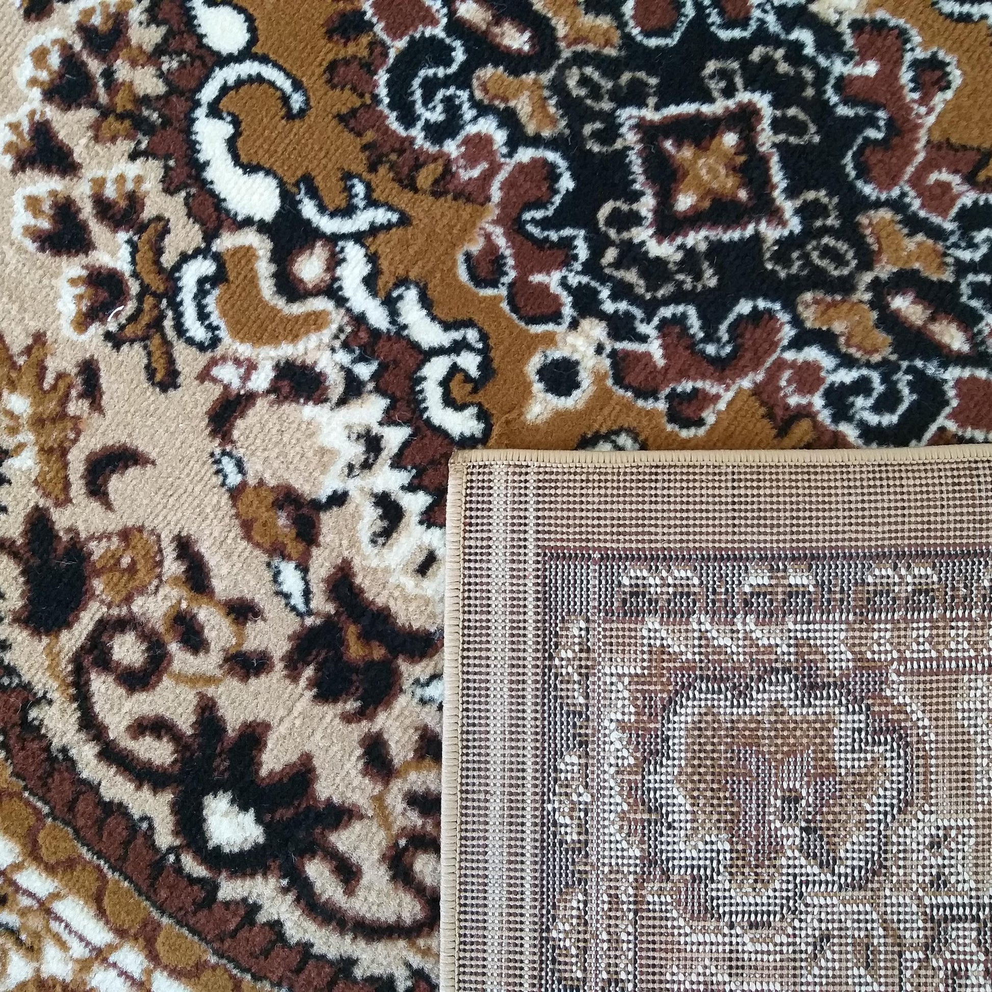 Tapis à motifs floraux et arabesques marron, noir et blanc cassé. Un coin est retourné, révélant le tissage du tapis