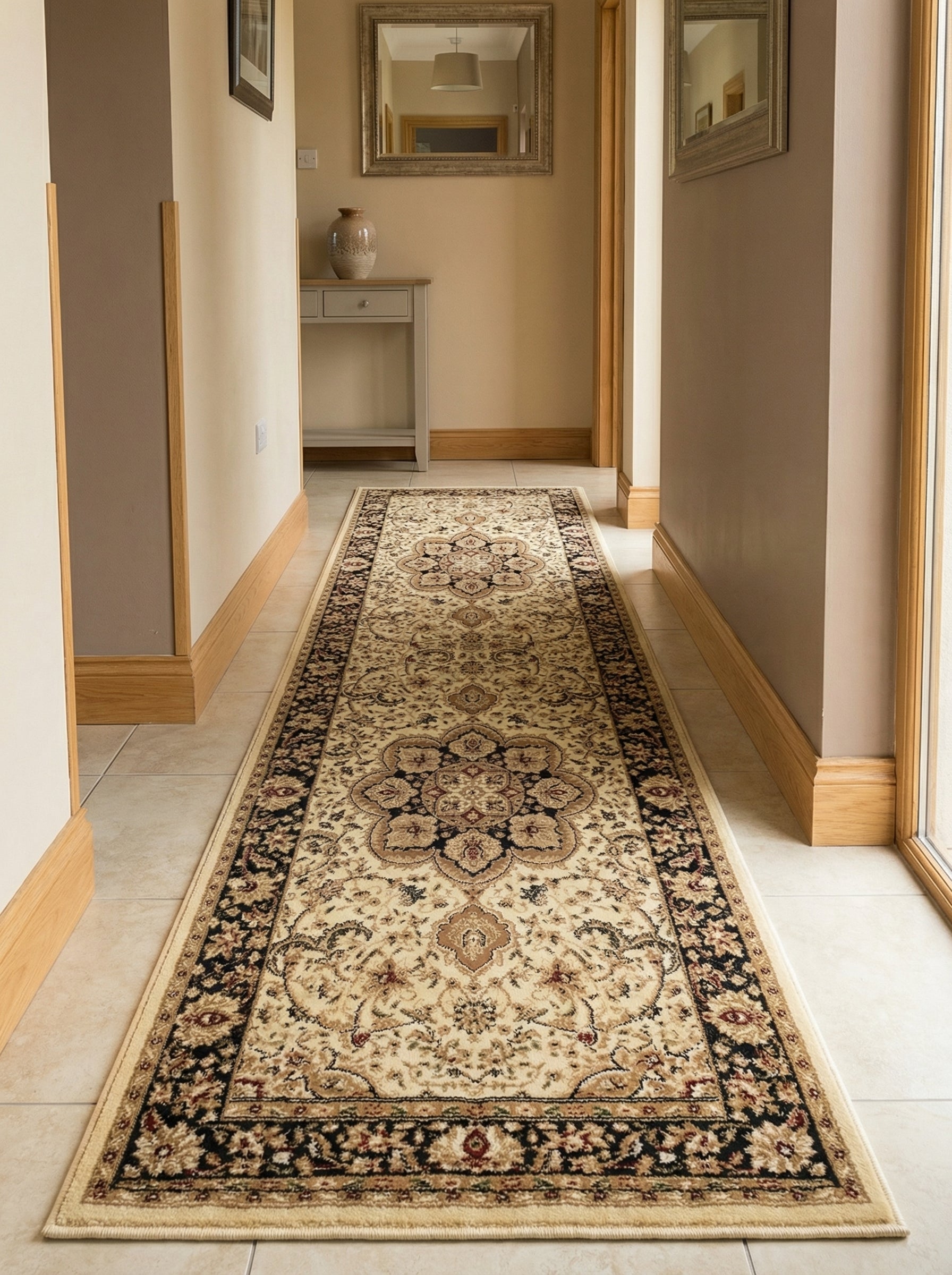 Un long chemin de tapis à motifs orientaux, crème, noir et bordeaux avec un médaillon central et une bordure foncée, posé sur un sol carrelé dans un couloir lumineux