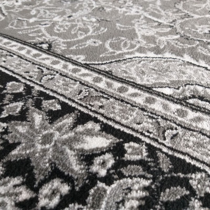 Tapis texturé aux motifs floraux et ornementaux, dominé par des tons de noir, gris clair et gris foncé, avec des détails blancs