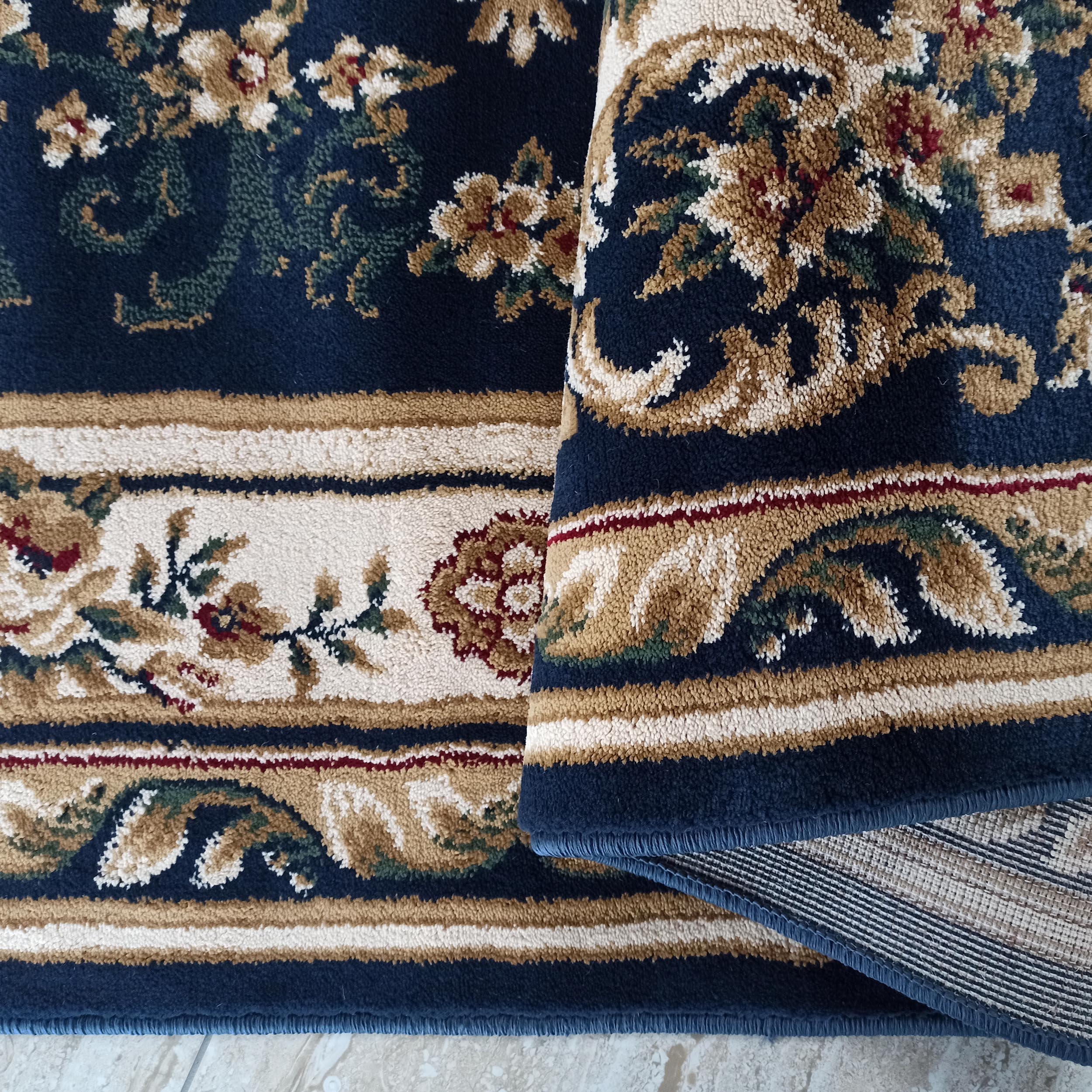 Tapis bleu foncé aux motifs floraux ornementaux crème, beiges, verts et bordeaux, dont la texture est douce et dense