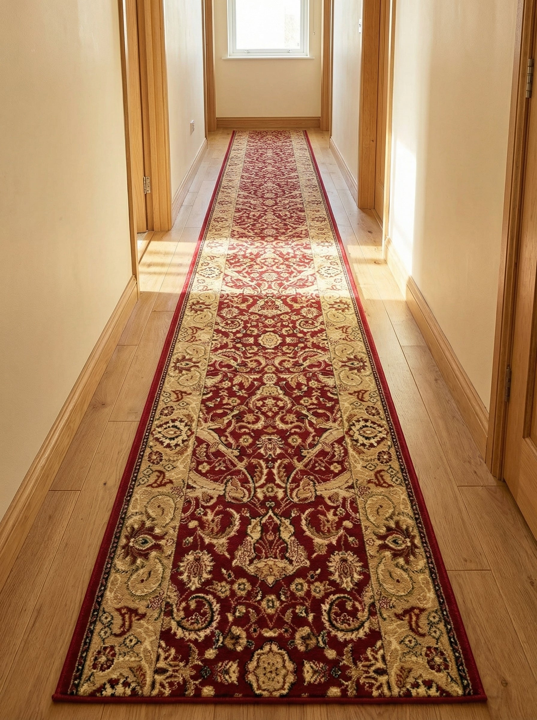 Long chemin de tapis rouge bordeaux et beige à motifs floraux et arabesques traditionnels, posé sur un parquet dans un couloir lumineux