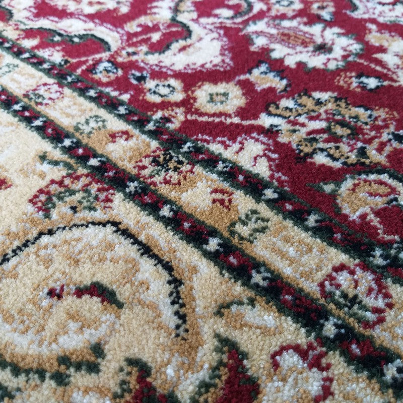 Tapis à motifs traditionnels avec des arabesques rouges, beiges et crème, bordé de lignes noires et vertes