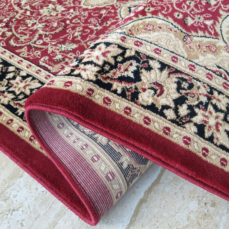 Tapis à motifs floraux et arabesques rouges, beiges et noirs, un pan est délicatement enroulé sur lui-même