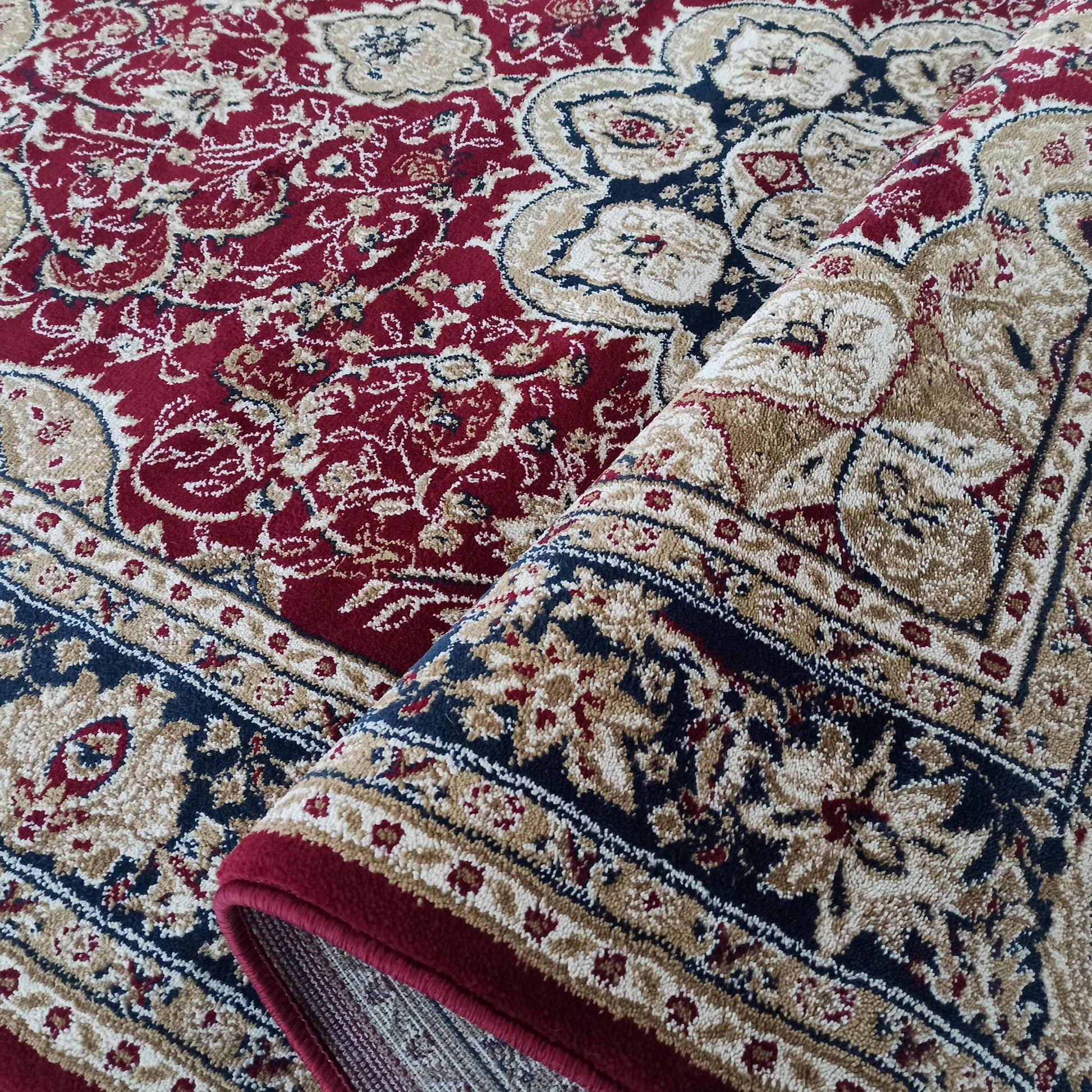 Tapis rouge bordeaux aux motifs floraux beiges, dorés et bleu marine, à la texture moelleuse, partiellement roulé
