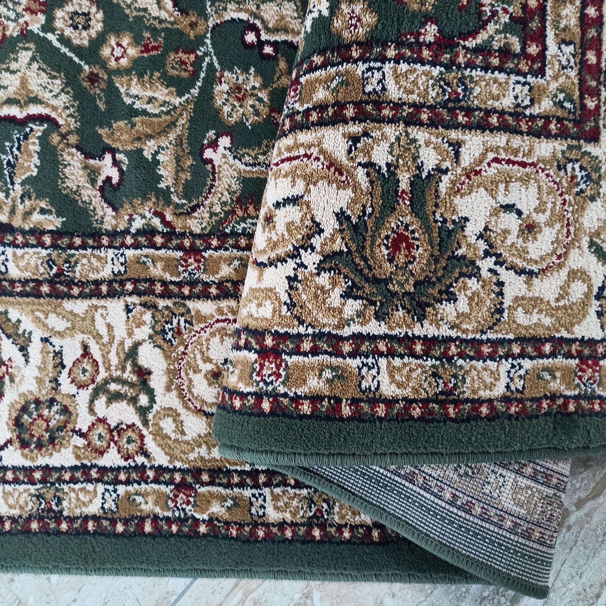 Tapis en textile vert foncé et crème aux motifs floraux traditionnels bordeaux et beiges, partiellement plié