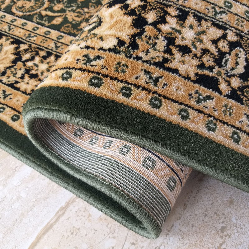 Tapis vert foncé, or et noir, aux motifs floraux et volutes classiques, bordure unie, enroulé sur un sol carrelé clair