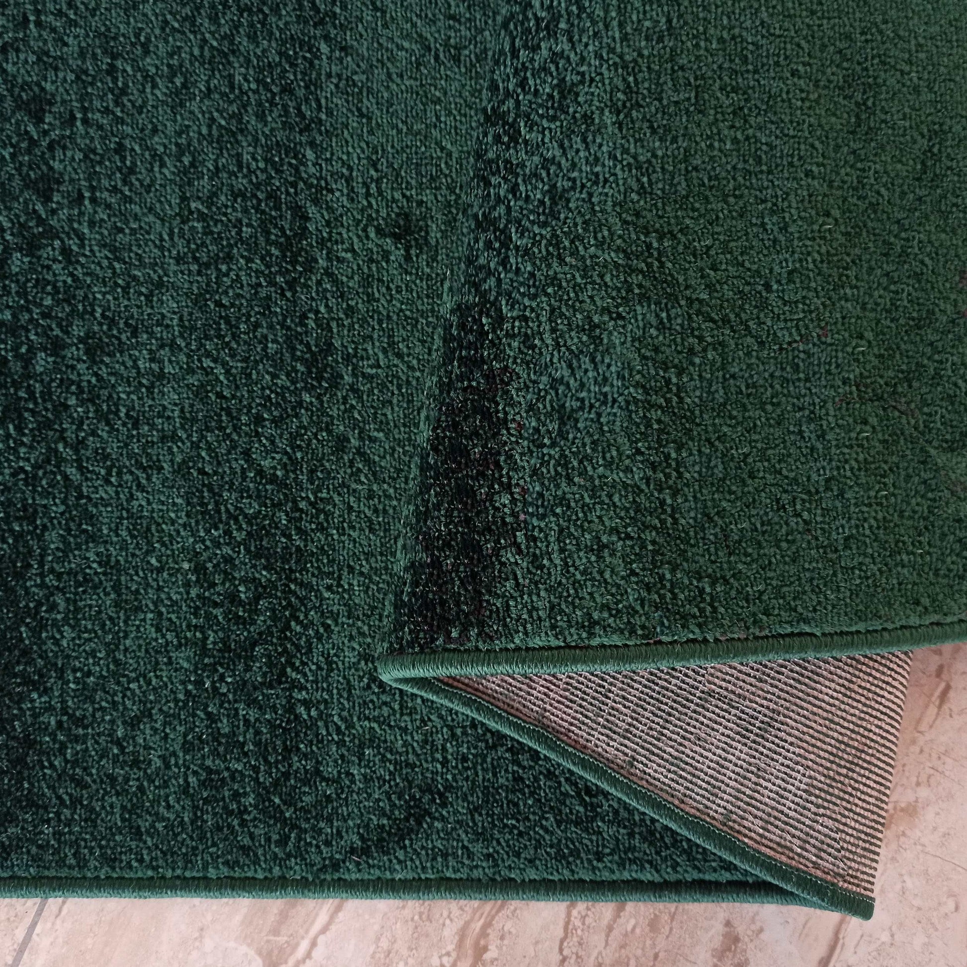 Tapis vert foncé moelleux, envers beige rayé tissé, bord surpiqué, sur sol clair