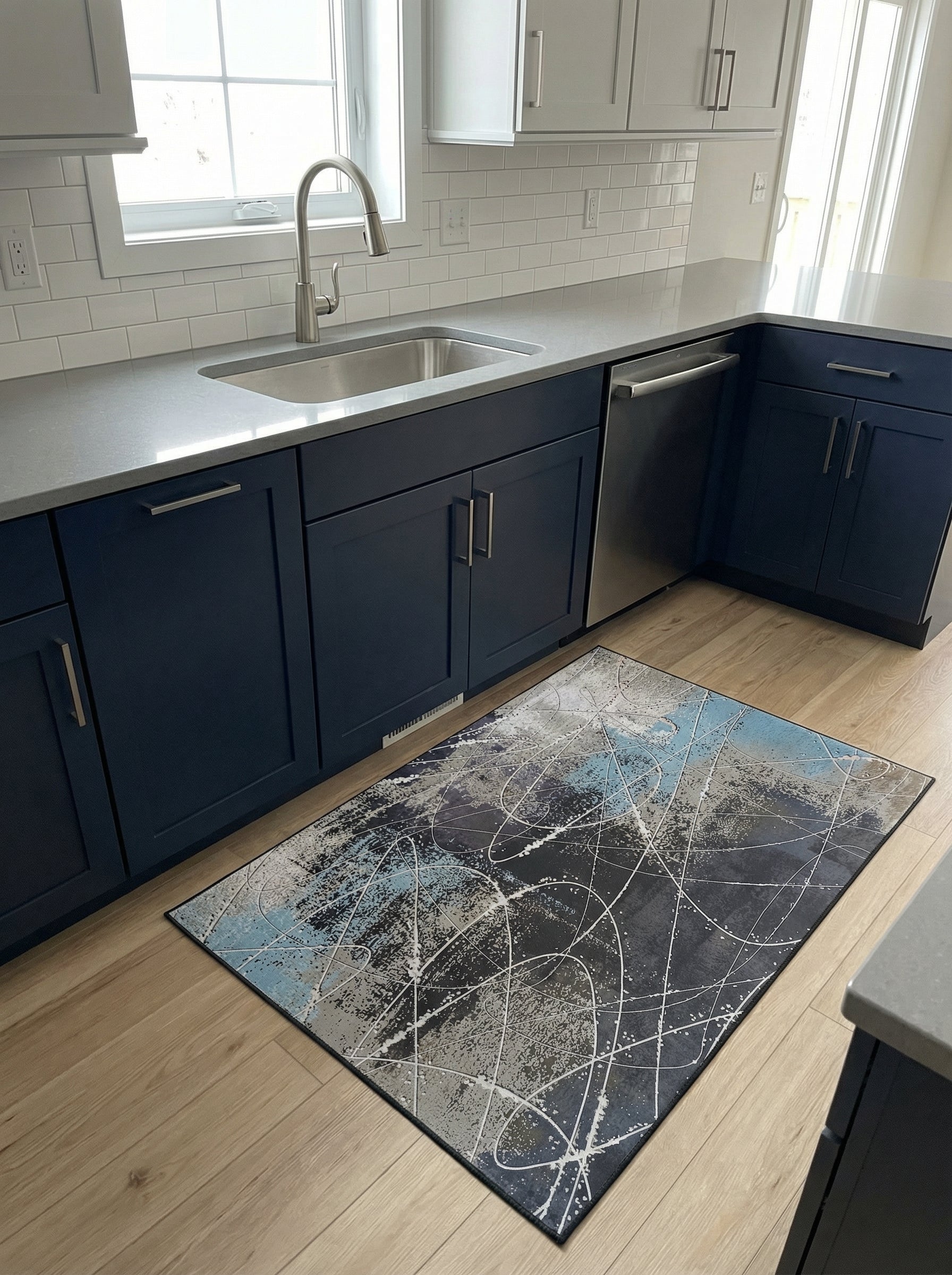 Tapis rectangulaire abstrait aux motifs gris foncé, bleu clair et blanc, posé sur un parquet en bois clair dans une cuisine moderne