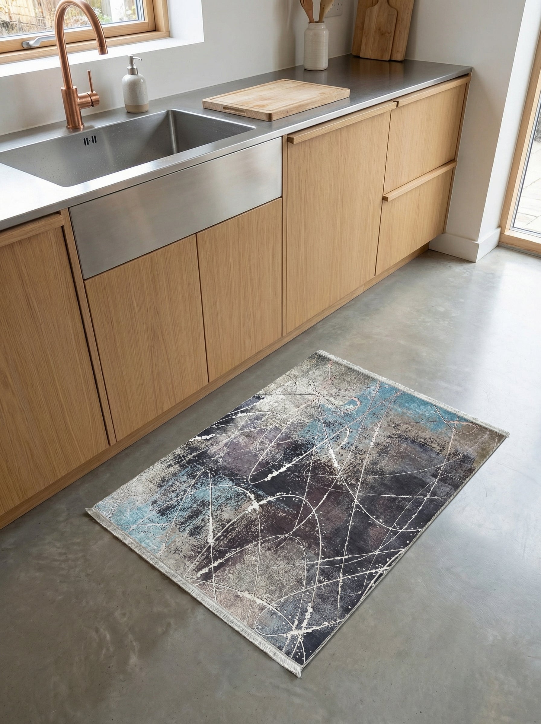 Tapis rectangulaire aux motifs abstraits de gris anthracite, bleu pétrole et touches blanches, posé sur un sol de cuisine en béton