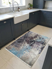 Tapis rectangulaire abstrait aux motifs éclaboussés de blanc, bleu, gris et noir, posé sur un sol carrelé dans une cuisine moderne
