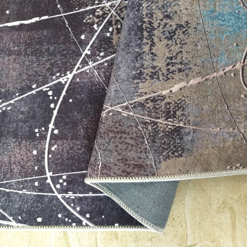 Tapis abstrait foncé avec motif cosmique de lignes blanches, taches beiges et bleues, plié montrant sa sous-face sur carrelage