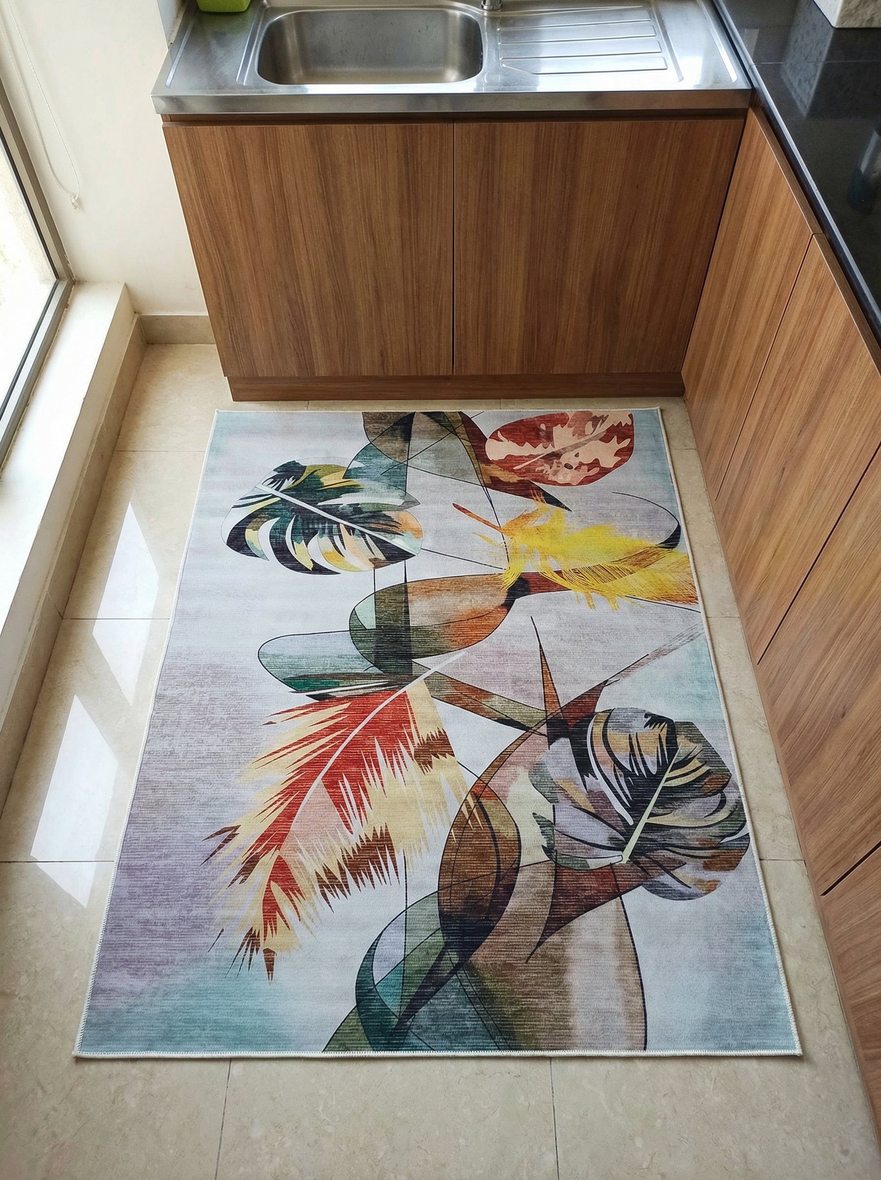 Tapis rectangulaire aux motifs abstraits de grandes feuilles colorées (verts, ocres, rouges, bleus) sur fond clair, dans une cuisine
