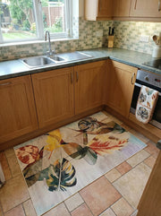 Tapis rectangulaire à motifs de feuilles tropicales stylisées aux couleurs vives (vert, jaune, orange, brun) sur fond clair, dans une cuisine