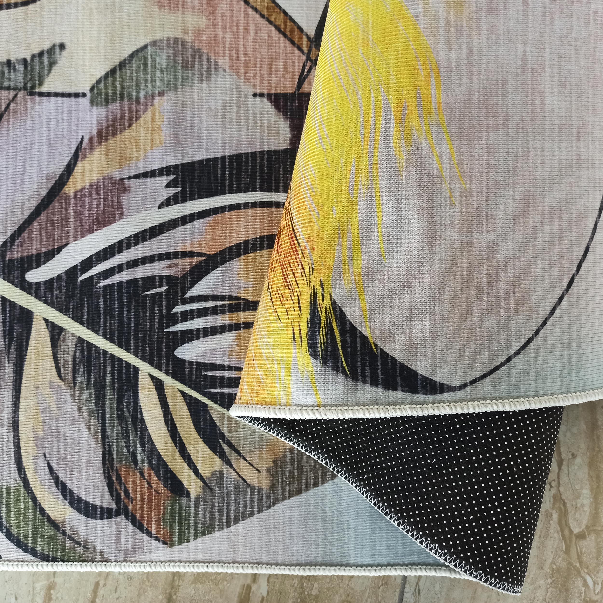 Tapis plié, motifs feuilles abstraites jaunes, noires, marron, vertes sur fond beige strié, bordure blanche, dos noir à pois blancs