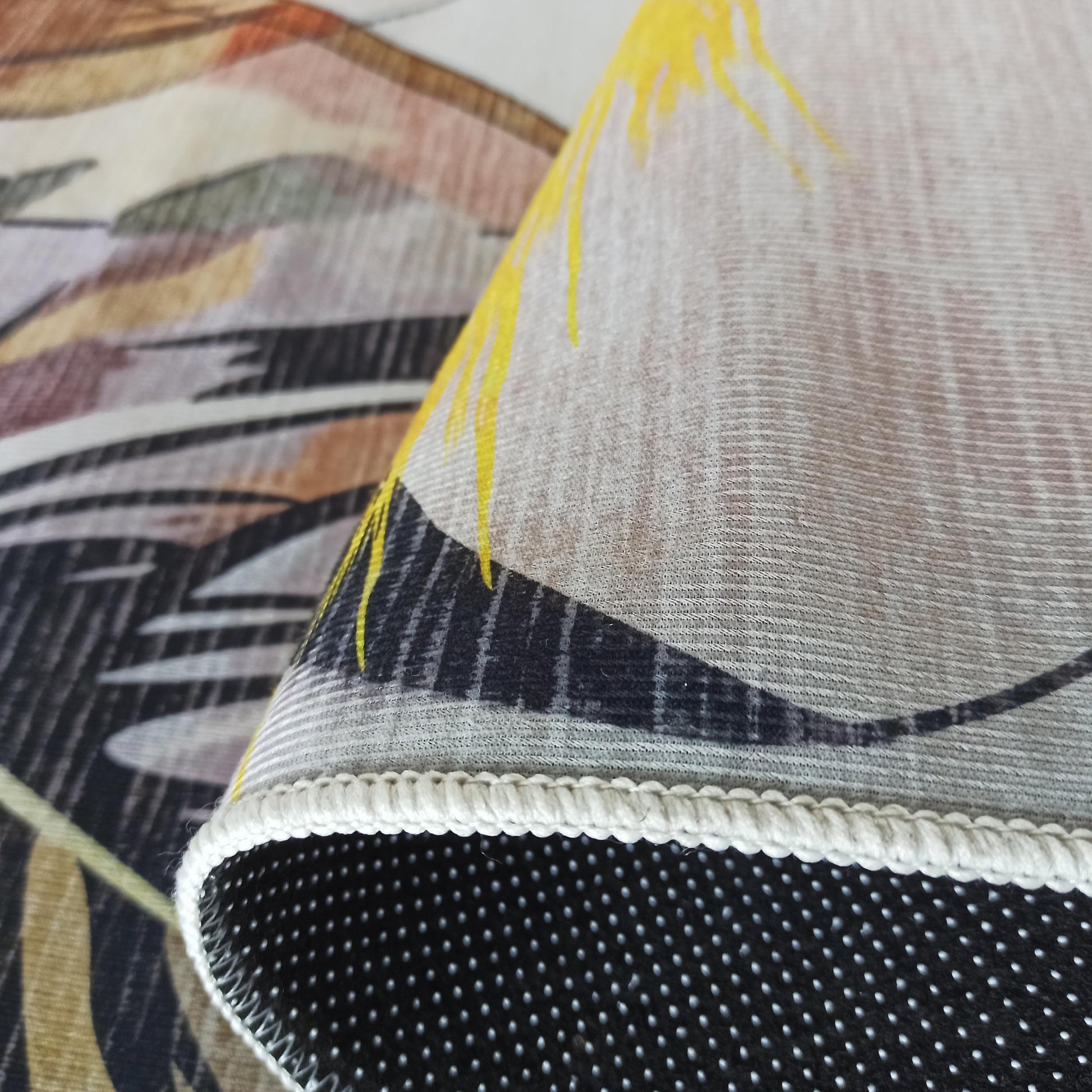Tapis replié affichant un motif abstrait jaune, noir et marron. Son envers antidérapant noir à pois blancs et sa finition claire sont visibles