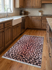 Tapis rectangulaire à motif léopard, taches sombres sur fond crème et rosé, bordé de franges claires, dans une cuisine lumineuse