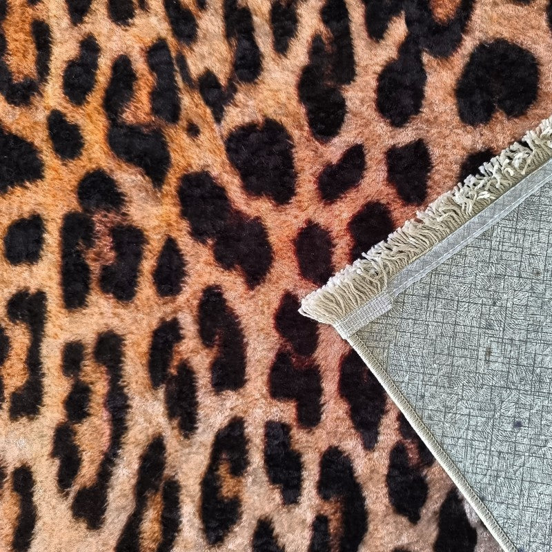 Tapis doux façon léopard noir et orangé. Un coin est replié, révélant une doublure grise quadrillée et des franges claires