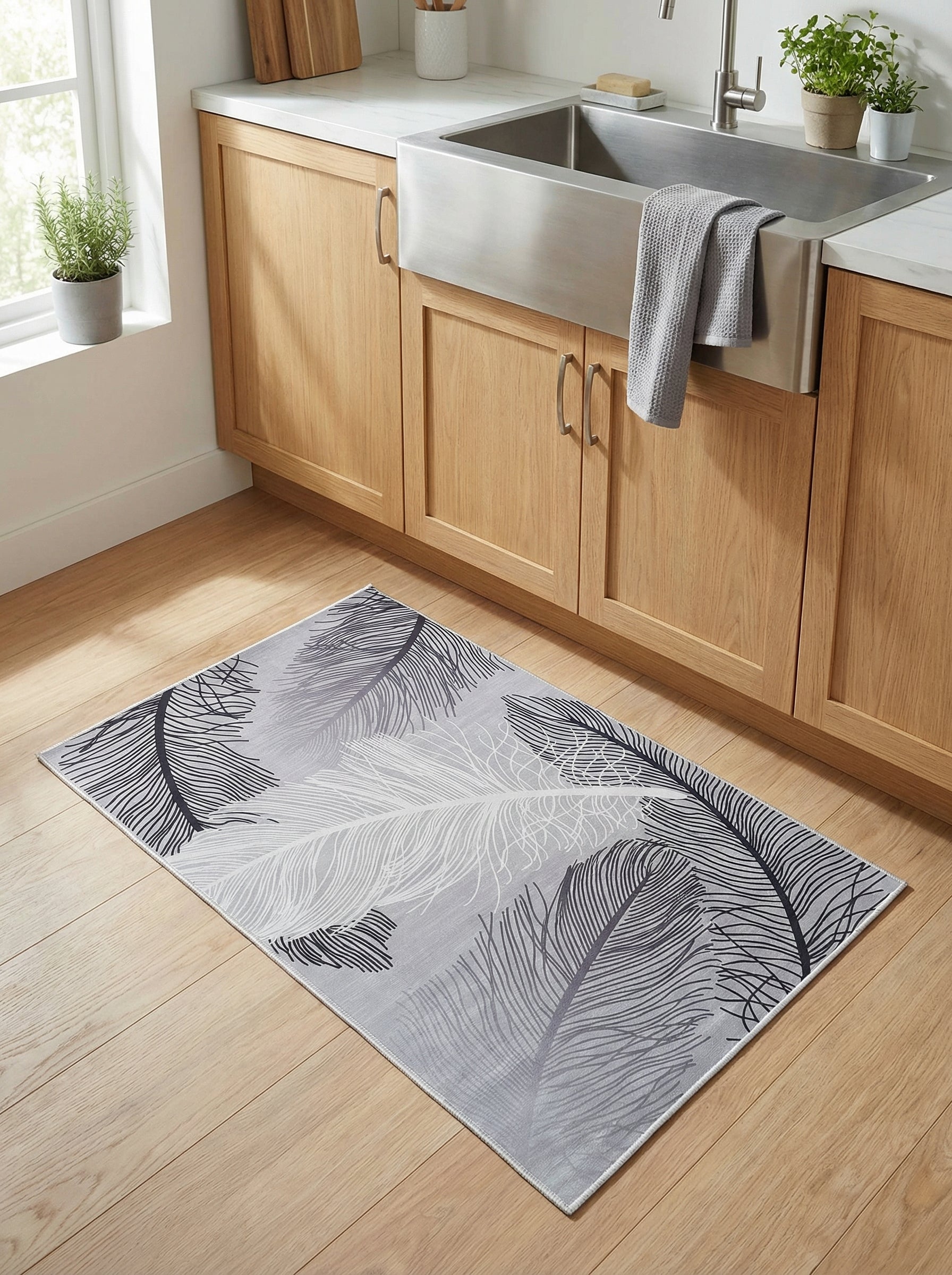 Tapis rectangulaire gris clair orné de grandes plumes noires, grises et blanches, posé sur un plancher en bois clair dans une cuisine moderne