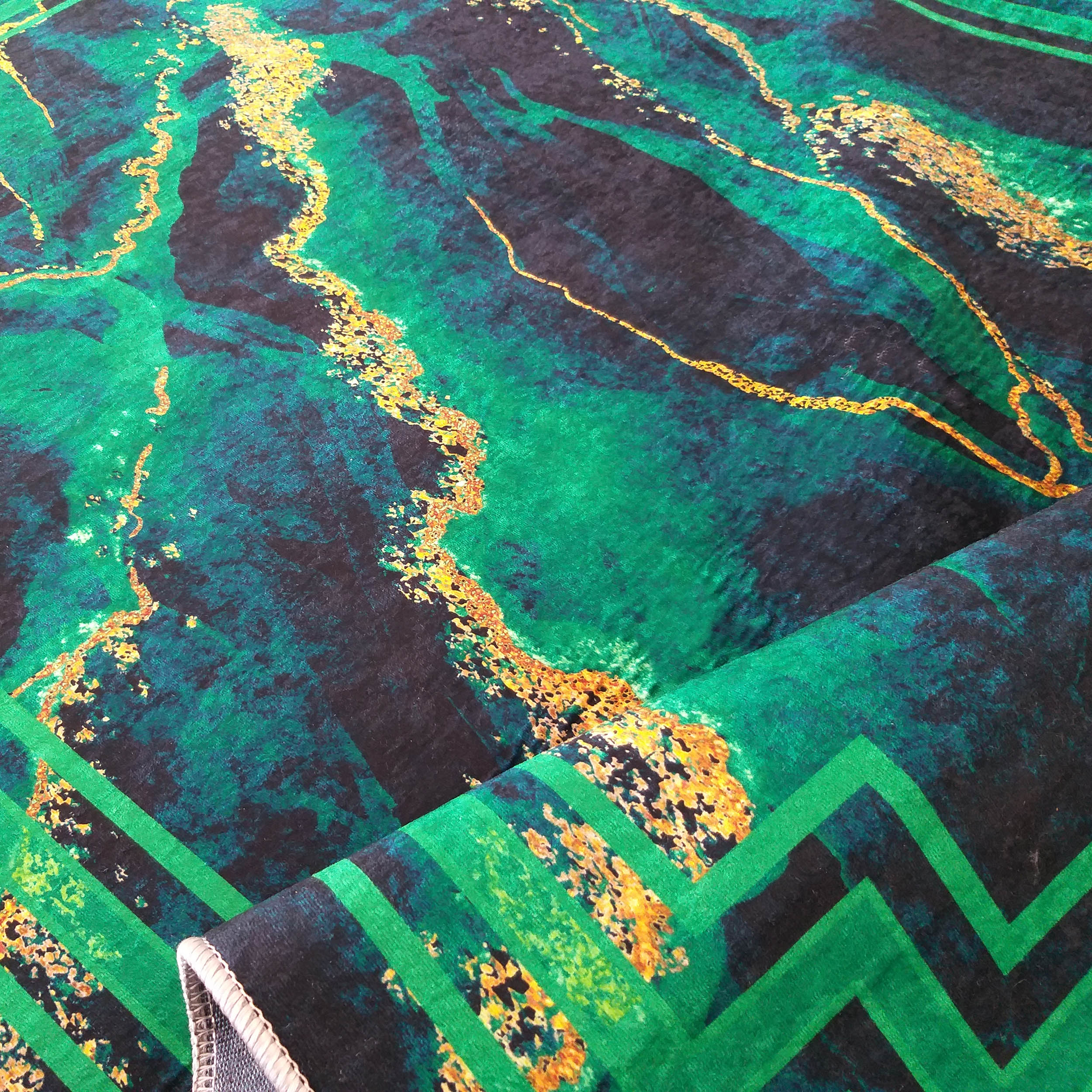 Tapis à motifs abstraits verts, noirs et dorés, avec un pan roulé révélant un bord et un motif géométrique vert