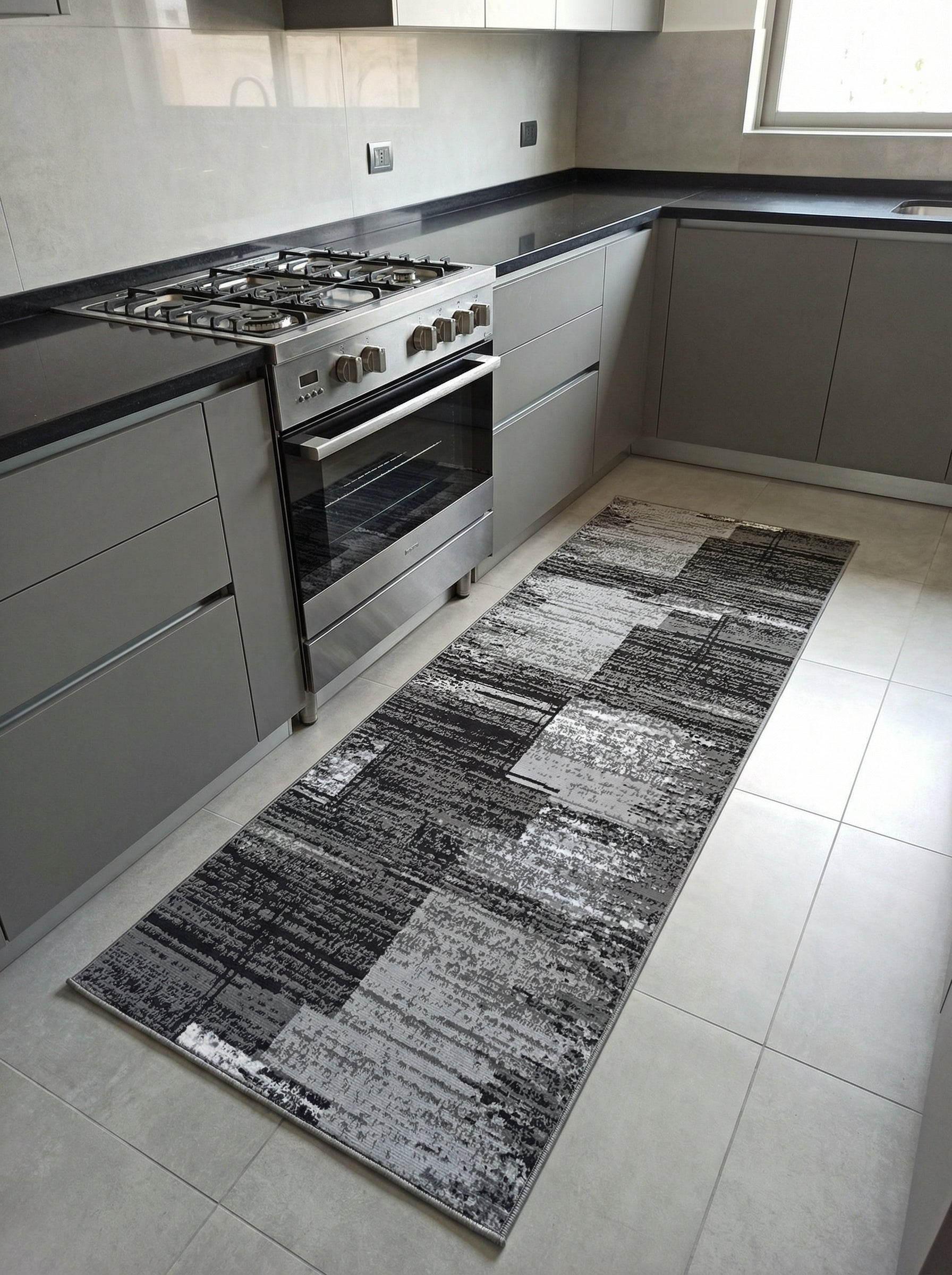 Tapis de couloir rectangulaire aux motifs abstraits texturés gris foncé, gris clair et noirs, posé sur le sol carrelé d'une cuisine moderne