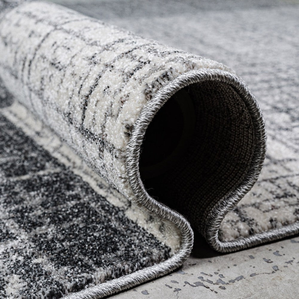 Gros plan sur un tapis texturé gris et blanc, partiellement roulé, avec des motifs abstraits