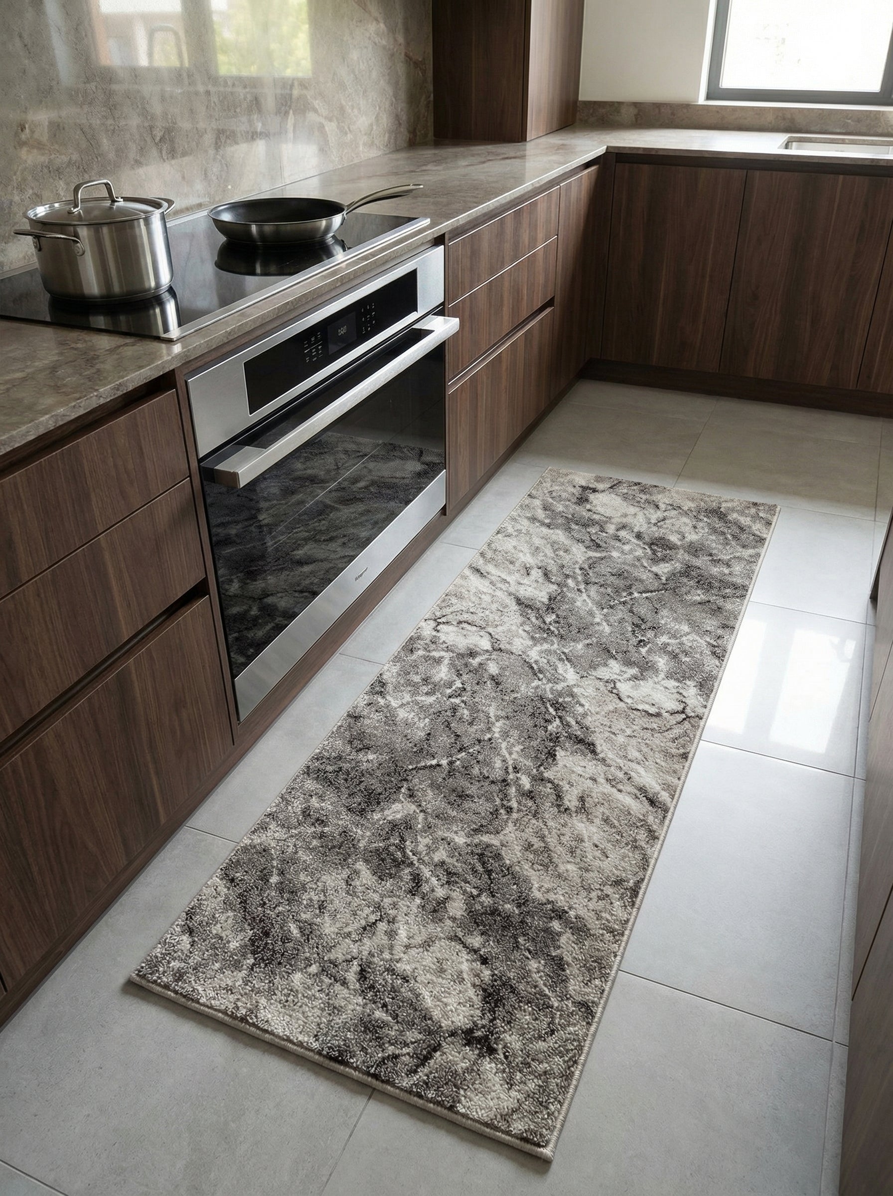 Tapis rectangulaire à poils longs aux motifs abstraits gris anthracite, gris clair et crème, posé sur un carrelage clair dans une cuisine moderne