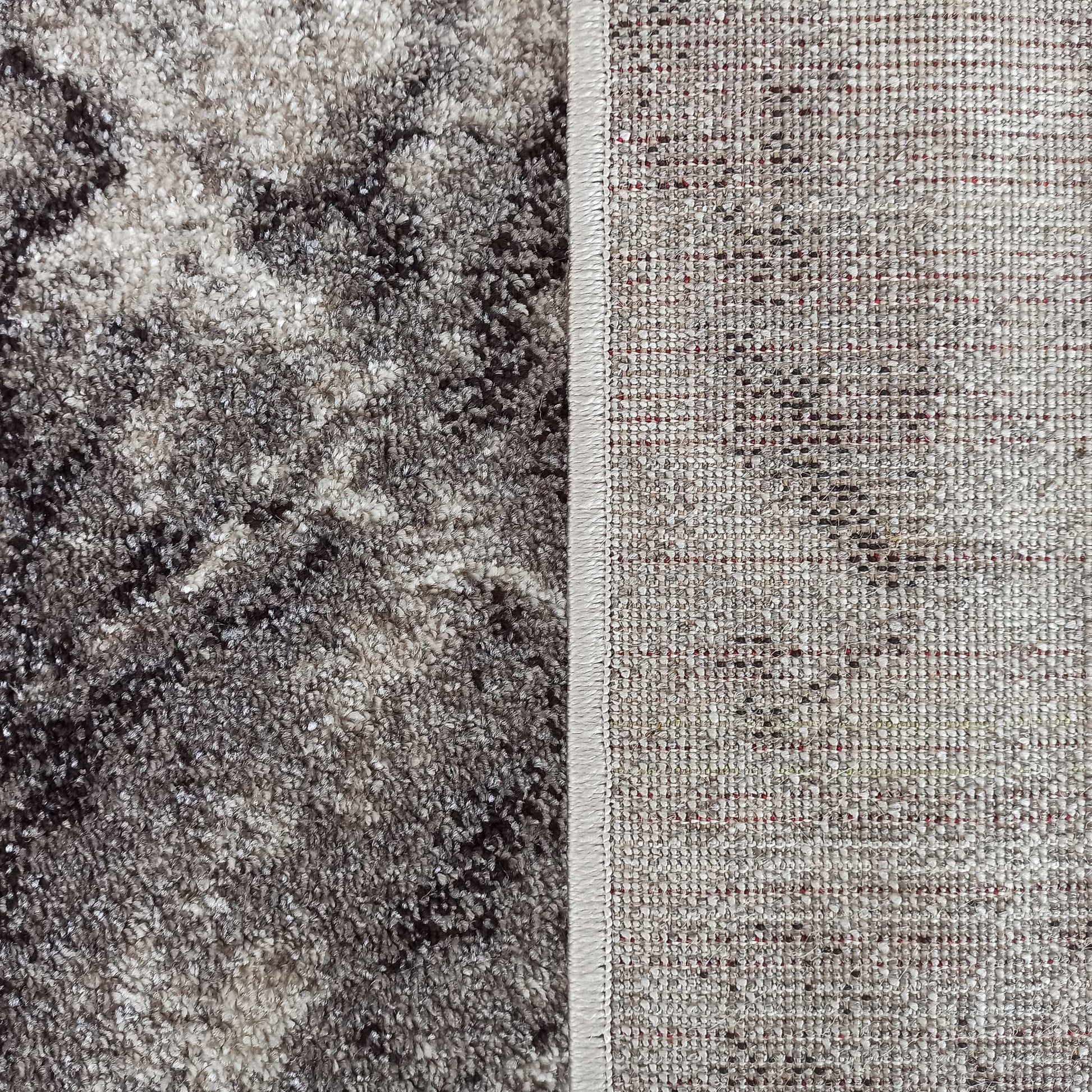 Gros plan sur un tapis montrant le dessus moelleux aux motifs abstraits gris et marron, et le dessous tissé clair à points rouges
