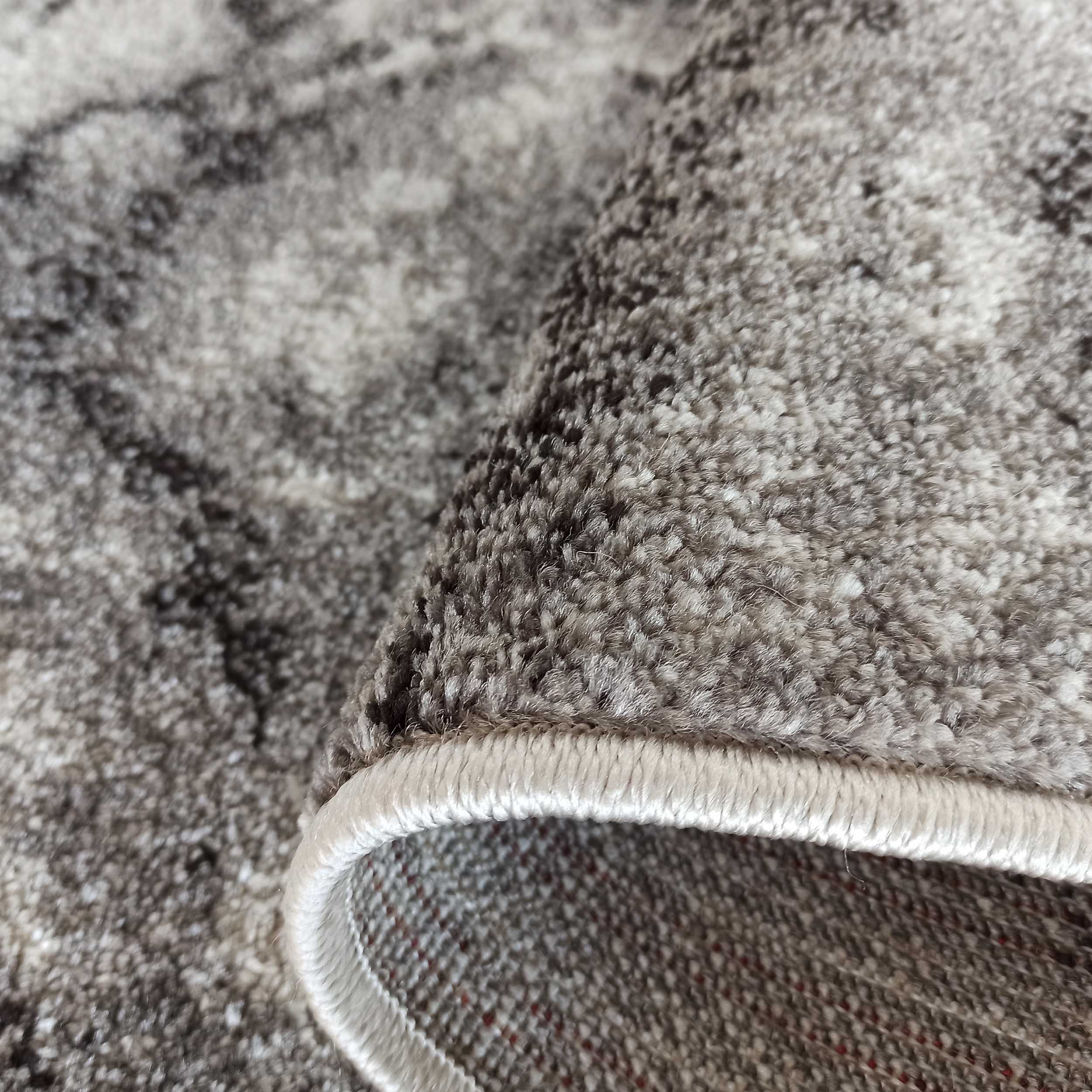 Gros plan d'un tapis aux tons gris et noirs avec un motif marbré, montrant la texture moelleuse et un bord roulé