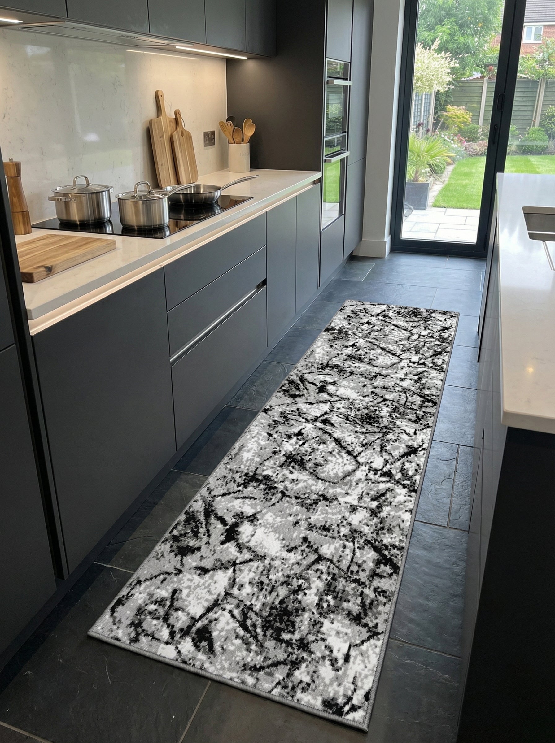 Tapis de couloir rectangulaire aux motifs graphiques noirs et gris sur fond blanc, posé sur un sol de cuisine moderne