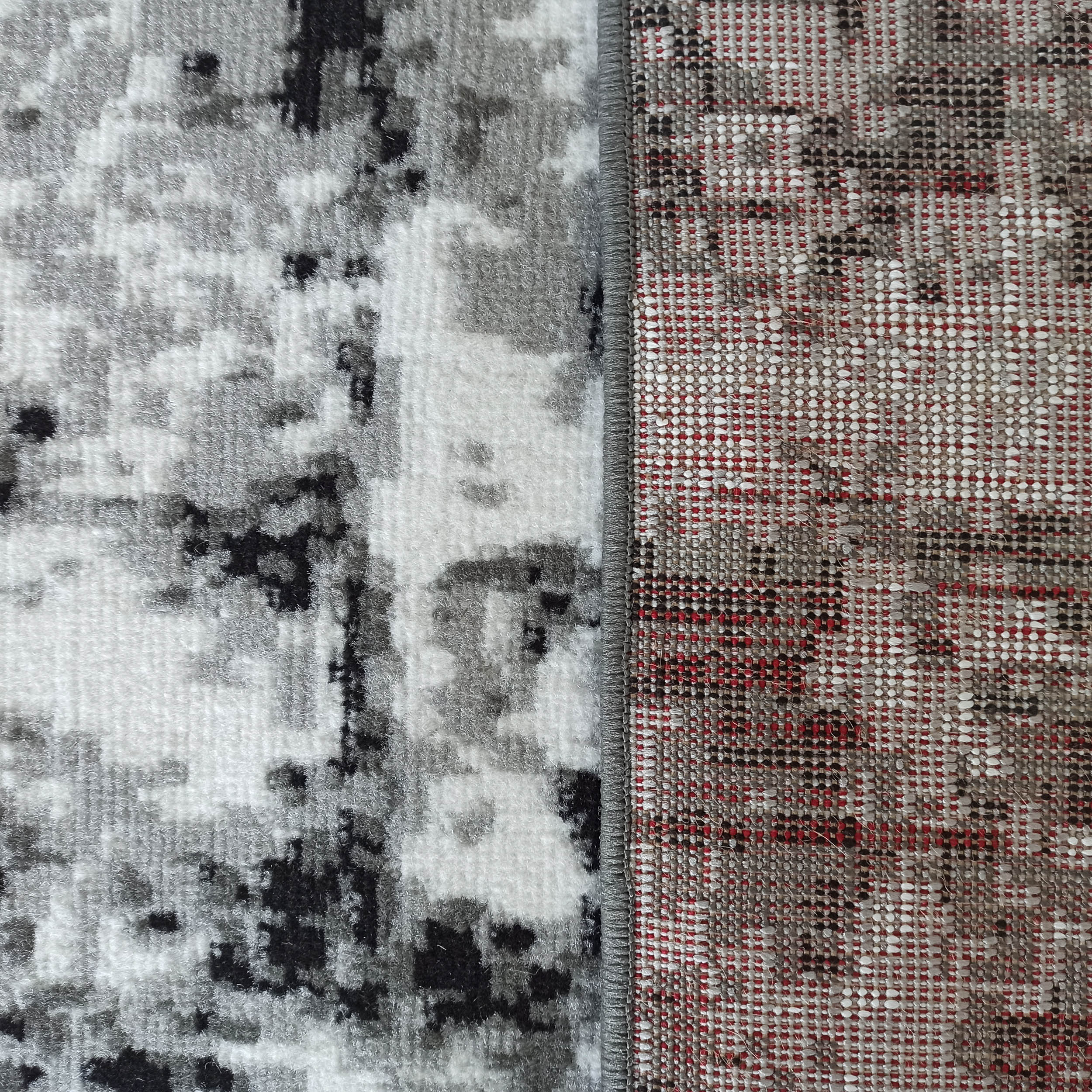 Tapis moelleux aux motifs abstraits gris, blancs et noirs, avec son envers tissé rouge, beige et gris, et un bord gris