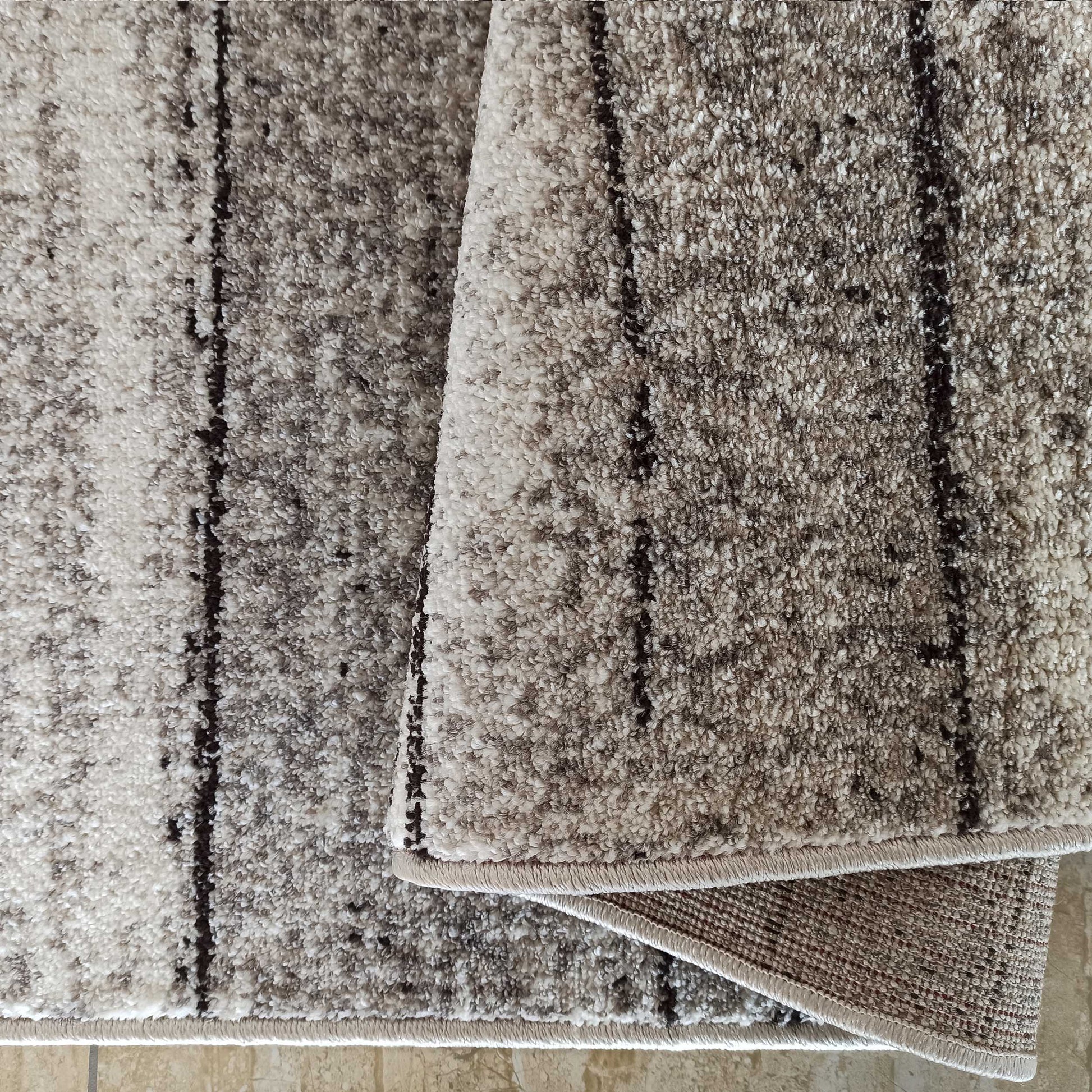 Tapis texturé à poils bouclés aux nuances de beige, gris et brun, avec des rayures foncées irrégulières, replié