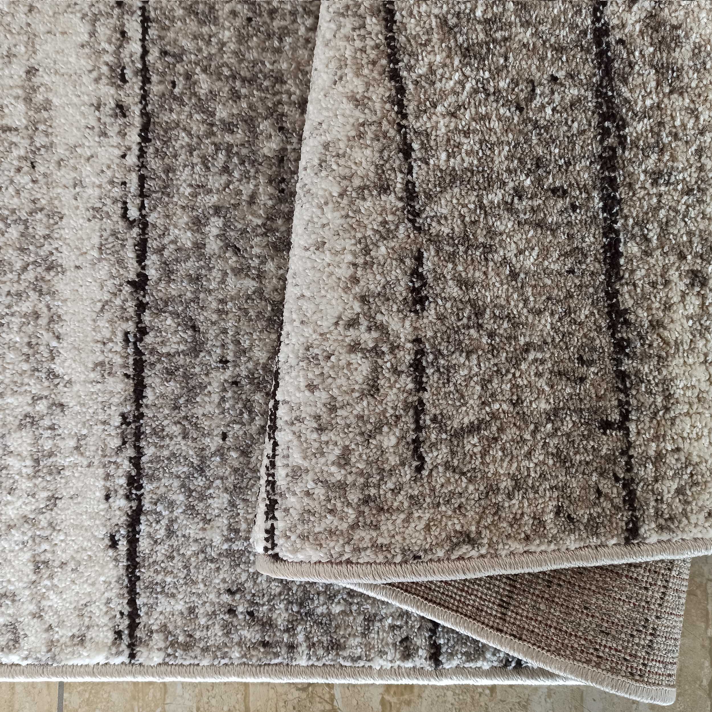 Tapis texturé à poils bouclés aux nuances de beige, gris et brun, avec des rayures foncées irrégulières, replié
