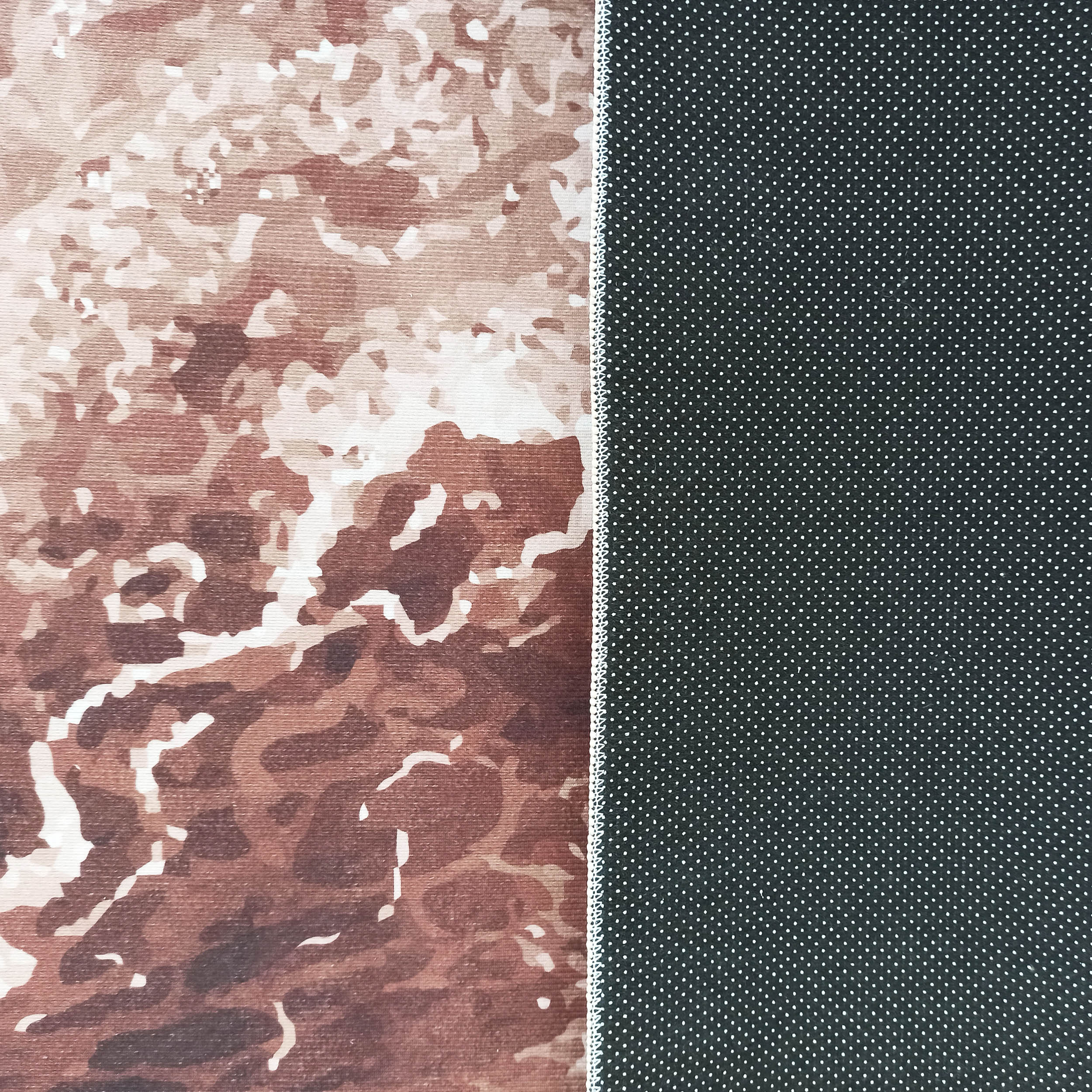 Le tapis montre sa face à motifs abstraits marron et crème et son dos noir à picots blancs antidérapants, séparés par une couture