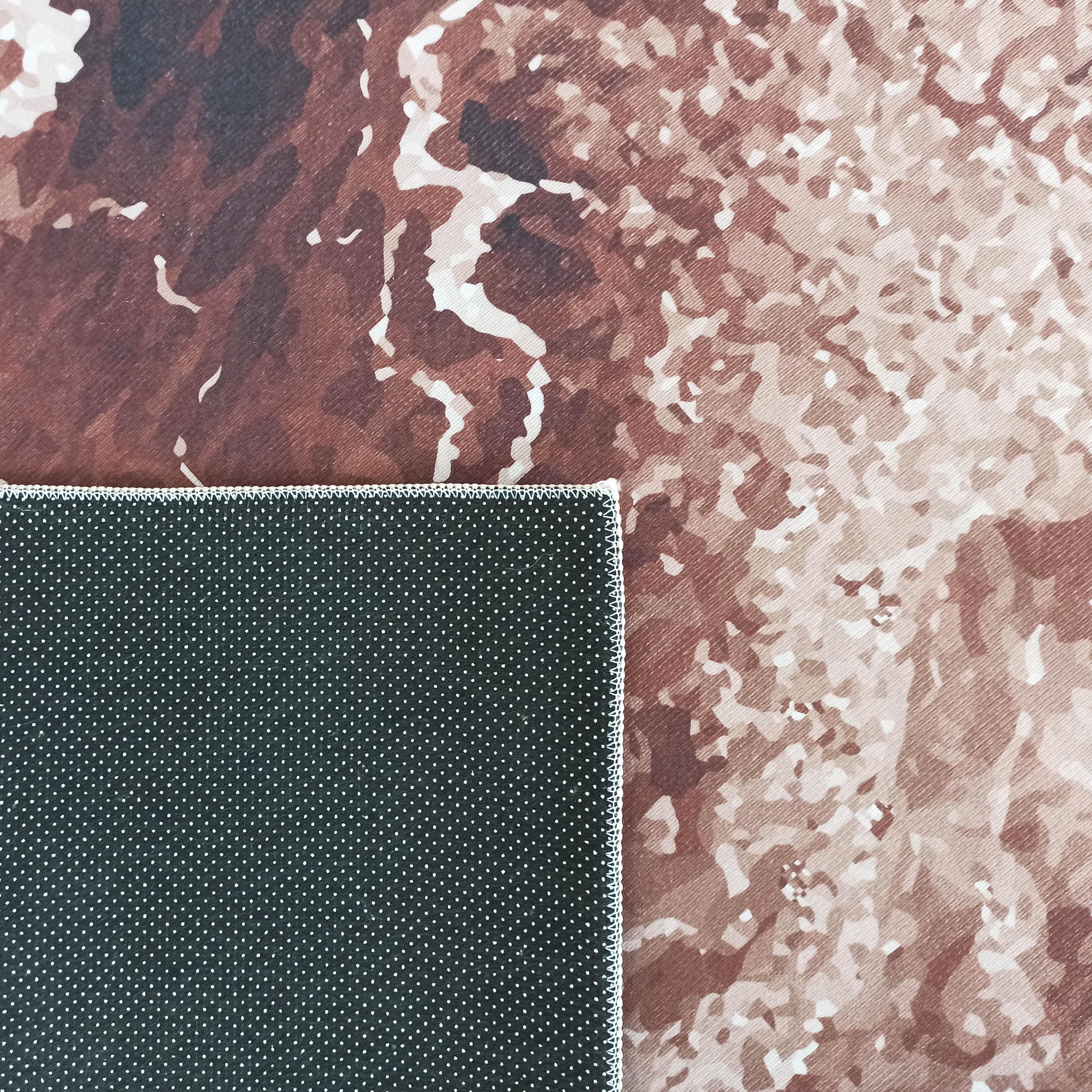 Tapis aux motifs abstraits marron, beige et blanc. Un coin du revers noir à pois blancs antidérapants est visible