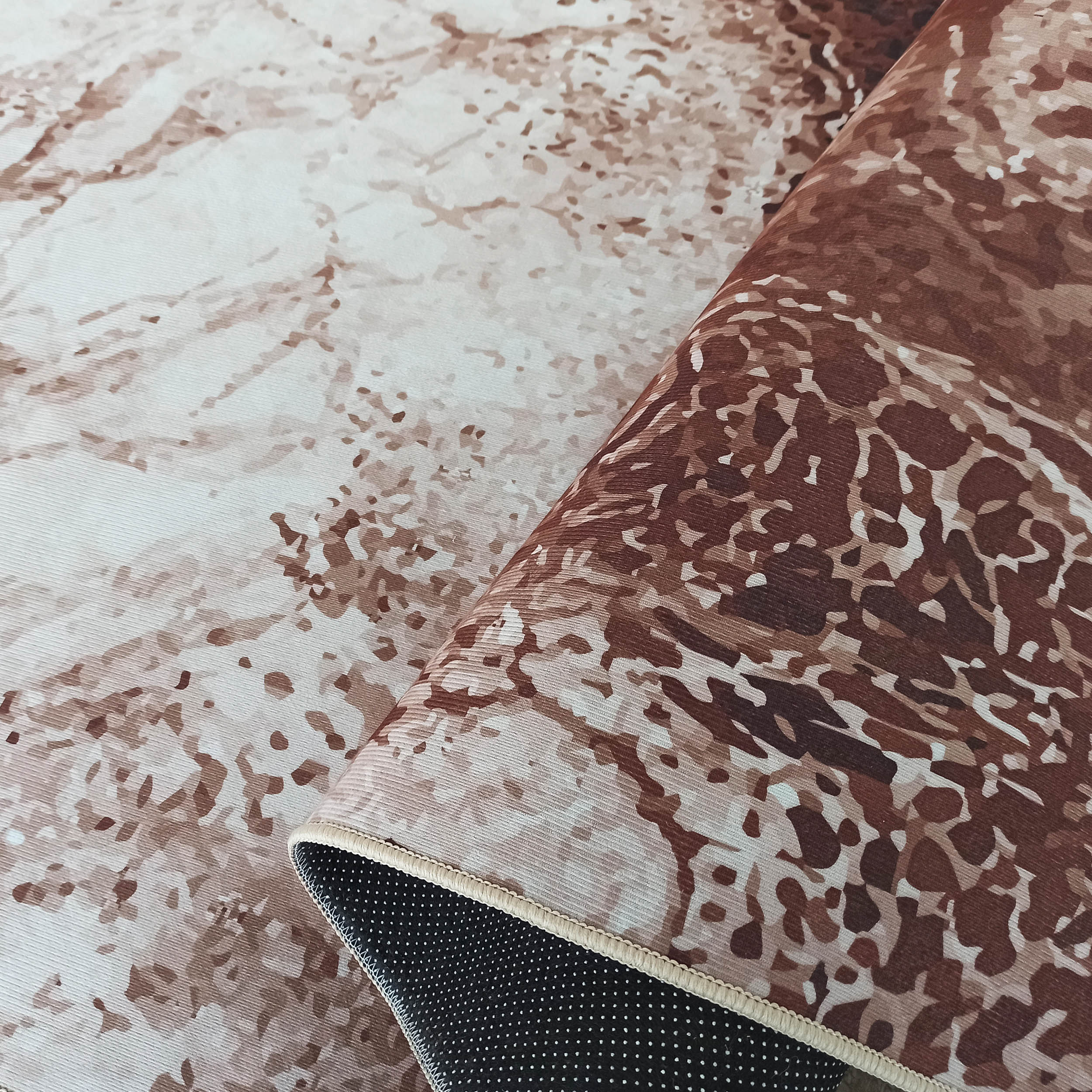 Tapis roulé avec motifs abstraits marron et beige clair, surface textile nervurée et envers noir à pois blancs