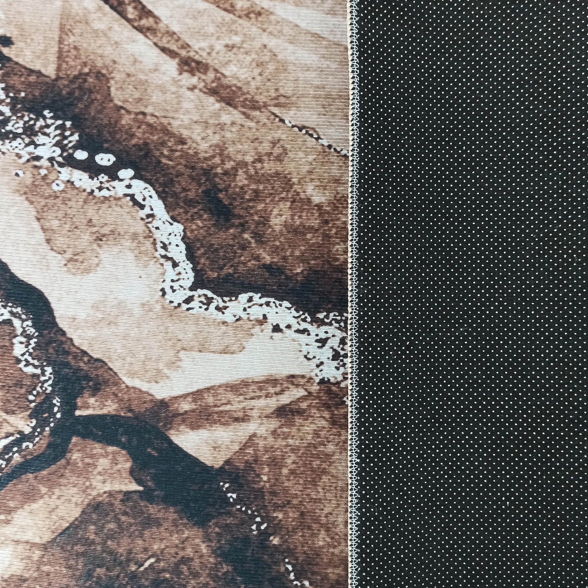 Tapis à surface marbrée marron et beige clair, bordé d'un dessous noir à petits pois blancs et d'une couture visible