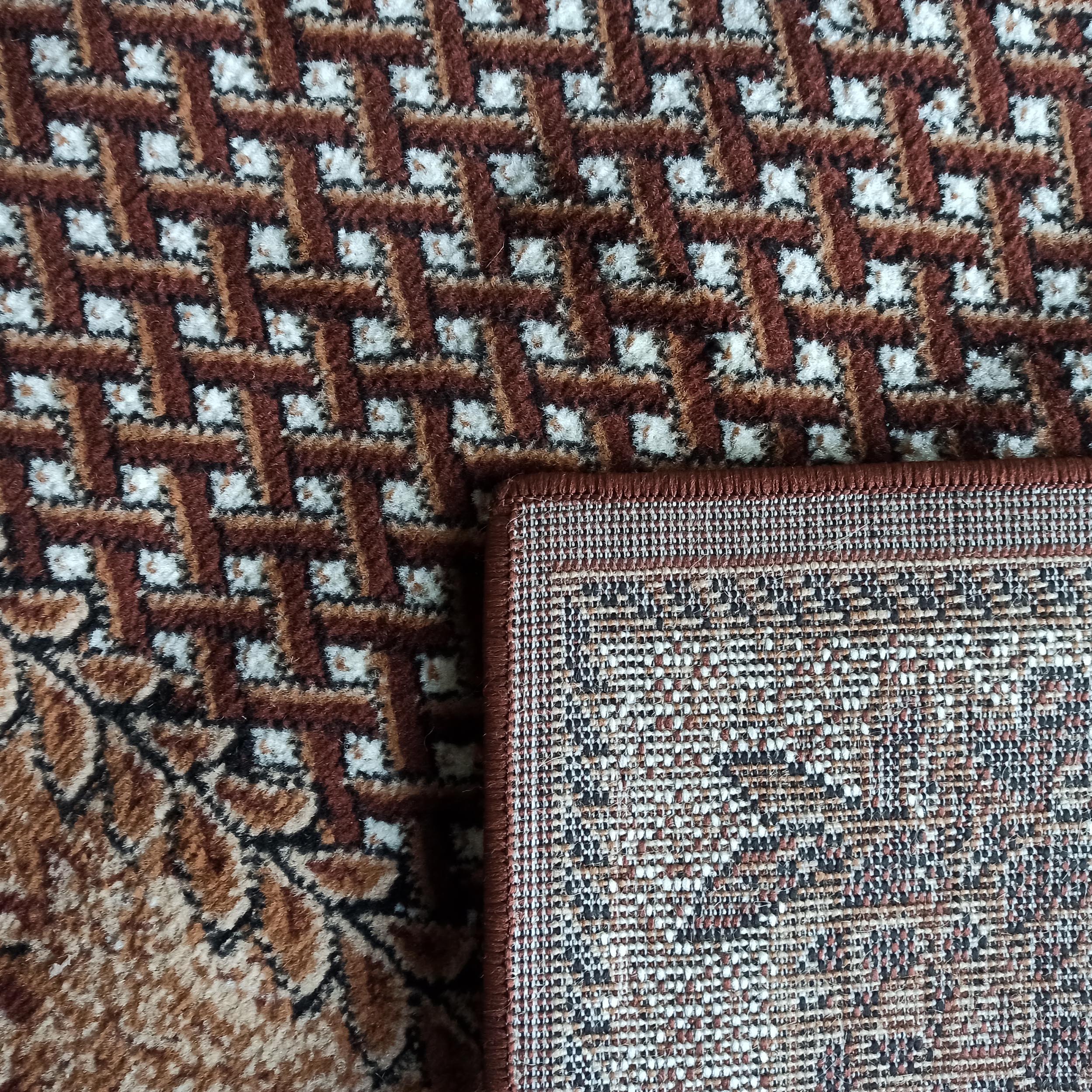 Tapis texturé marron, blanc et noir avec motifs géométriques et floraux. Un coin relevé dévoile l'envers tissé