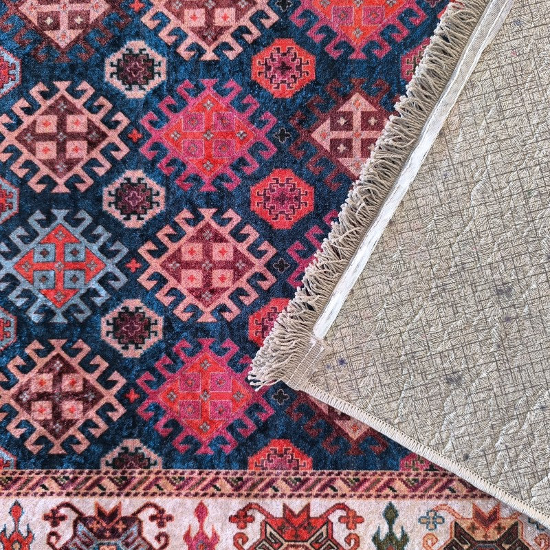 Tapis à motifs géométriques bleu foncé, rouge fuchsia et beige, avec une bordure décorée et son revers visible avec franges