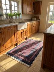 Tapis rectangulaire à motifs orientaux rouges et bleus foncés avec des franges blanches, posé sur un sol carrelé dans une cuisine ensoleillée