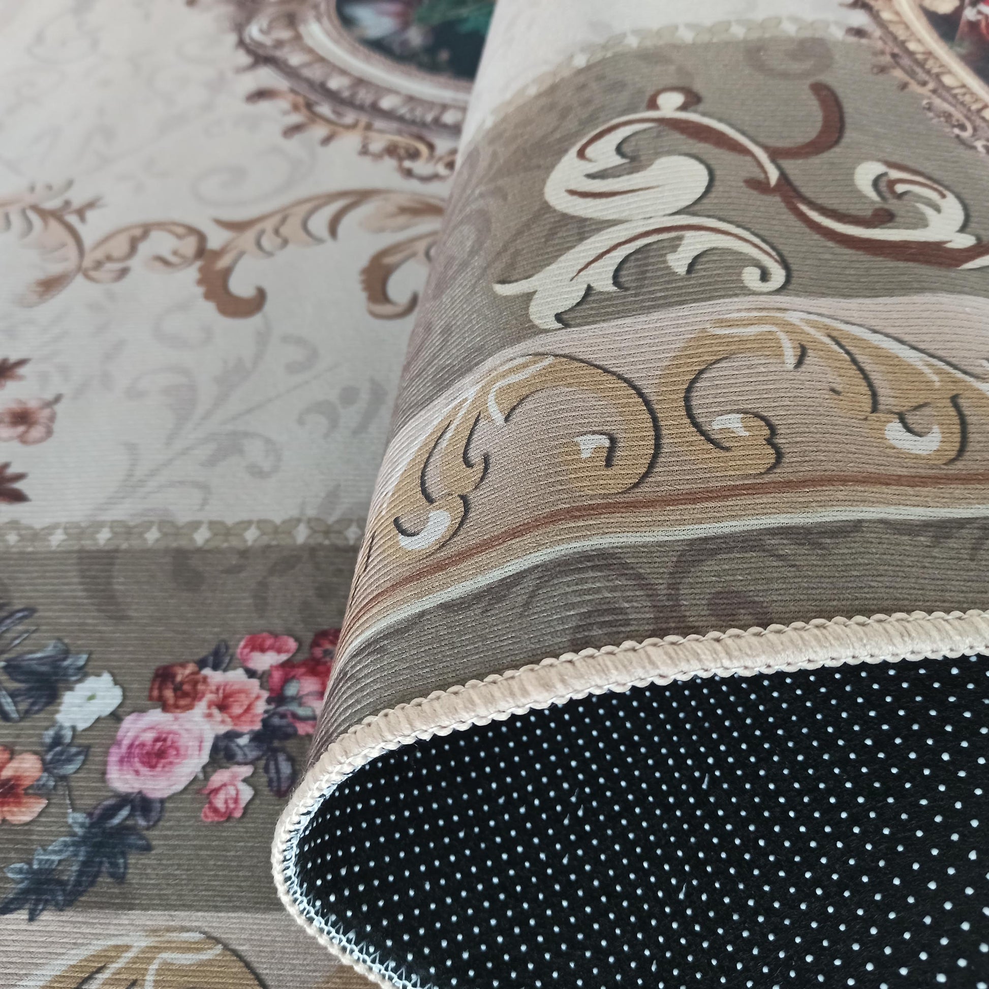 Tapis partiellement roulé, orné de motifs floraux beiges, marron et roses sur la face supérieure et un dessous noir à pois blancs, bordé d'une tresse beige