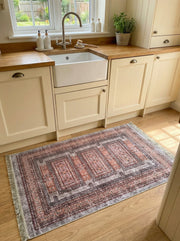 Tapis rectangulaire aux motifs ethniques gris, rouille et noir avec franges claires, posé sur un plancher en bois dans une cuisine lumineuse