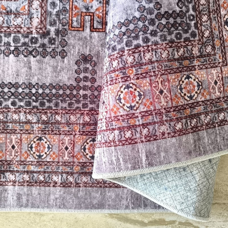 Tapis moelleux gris à motifs géométriques et floraux traditionnels orangés et rouges, partiellement roulé pour montrer son envers texturé clair